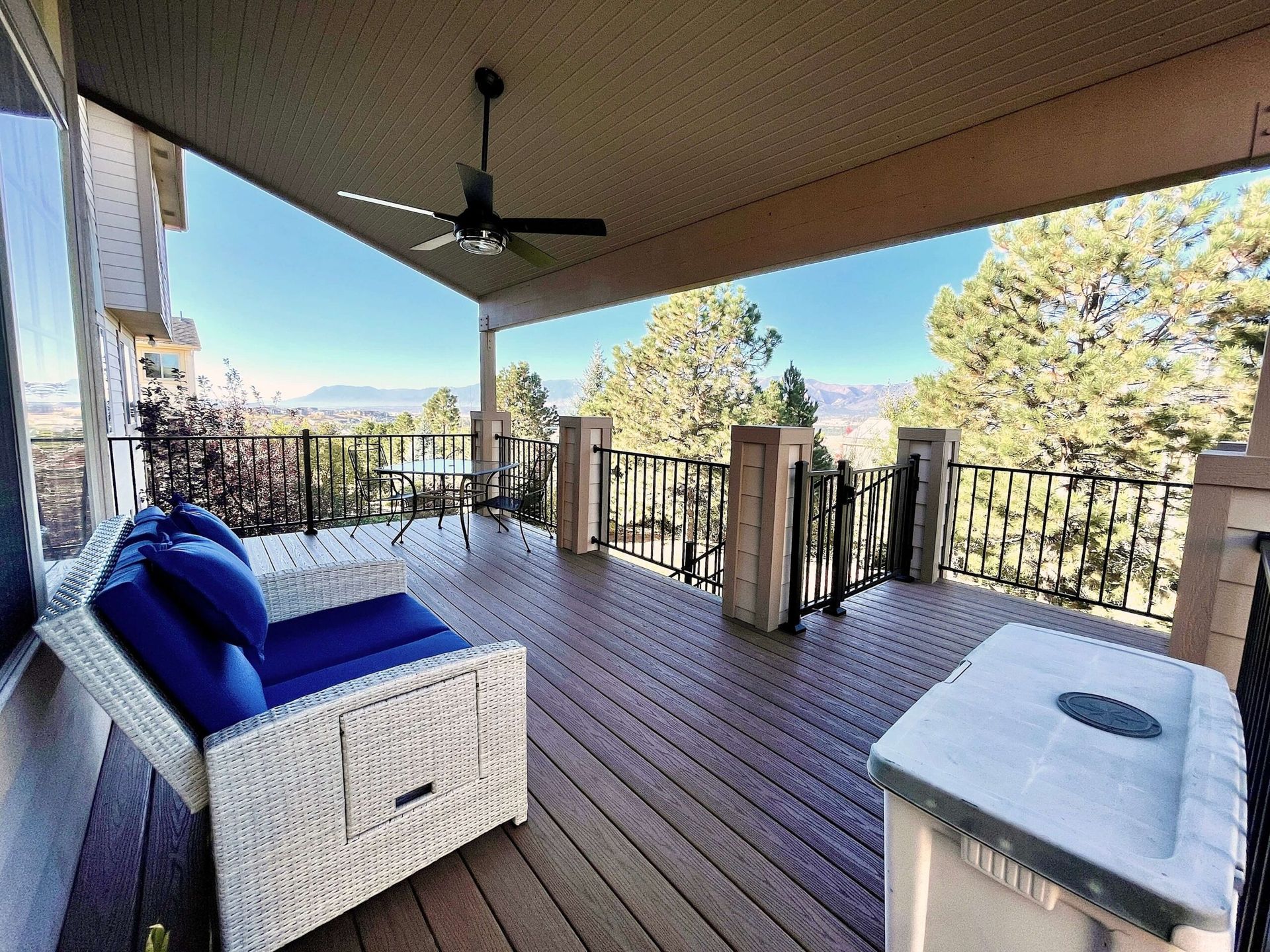 Covered deck with blue cushioned sofa, table, and scenic view.