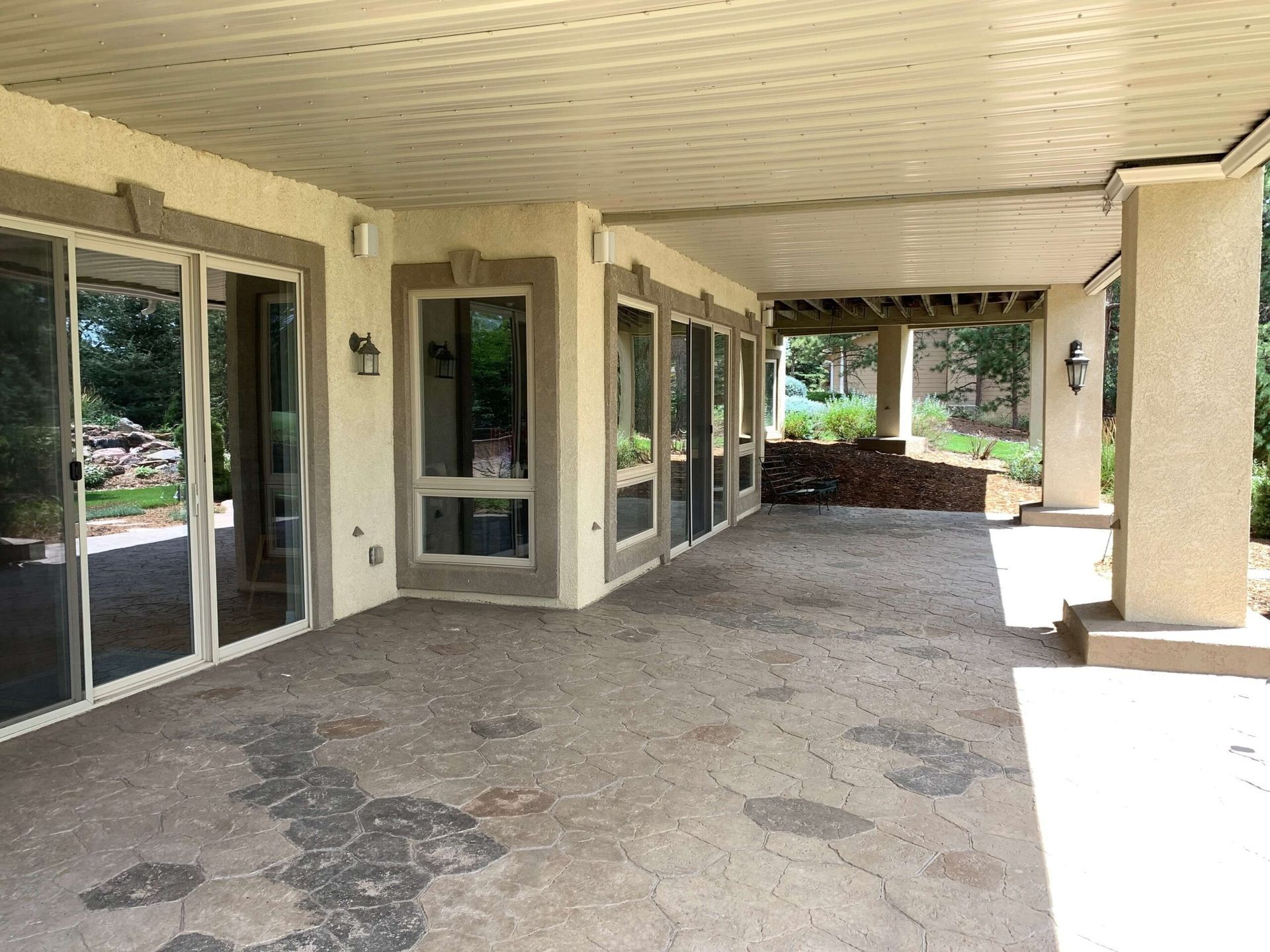 Covered patio with multiple glass doors, stone flooring, and beige walls.