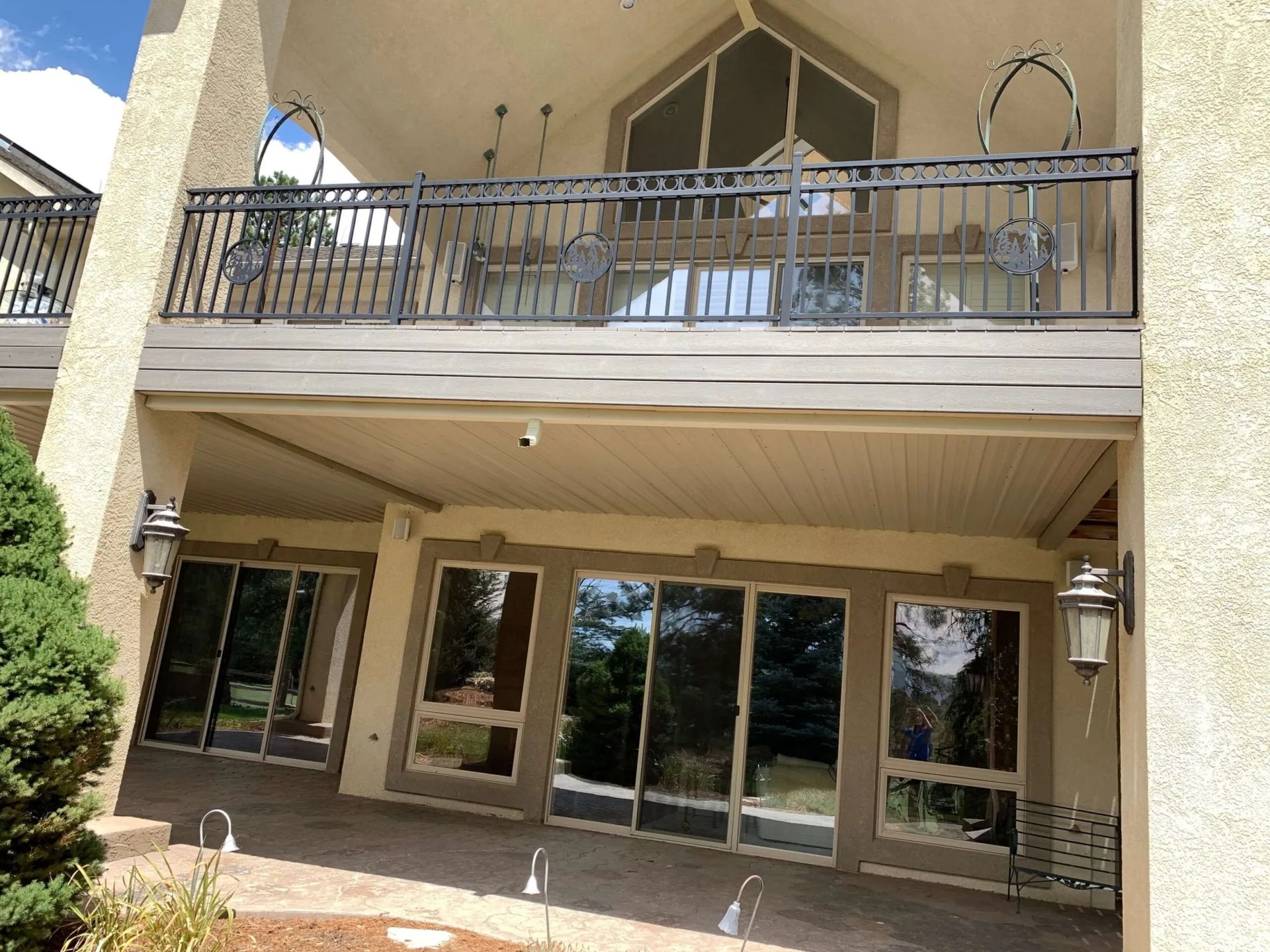 Two-story house with a balcony and sliding glass doors. Brown brick patio and green bush.