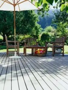 Wooden deck with outdoor furniture, umbrella, and a basket of flowers in a garden setting.