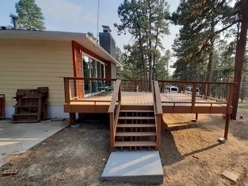 Wooden deck with stairs attached to a light yellow house in a wooded area.