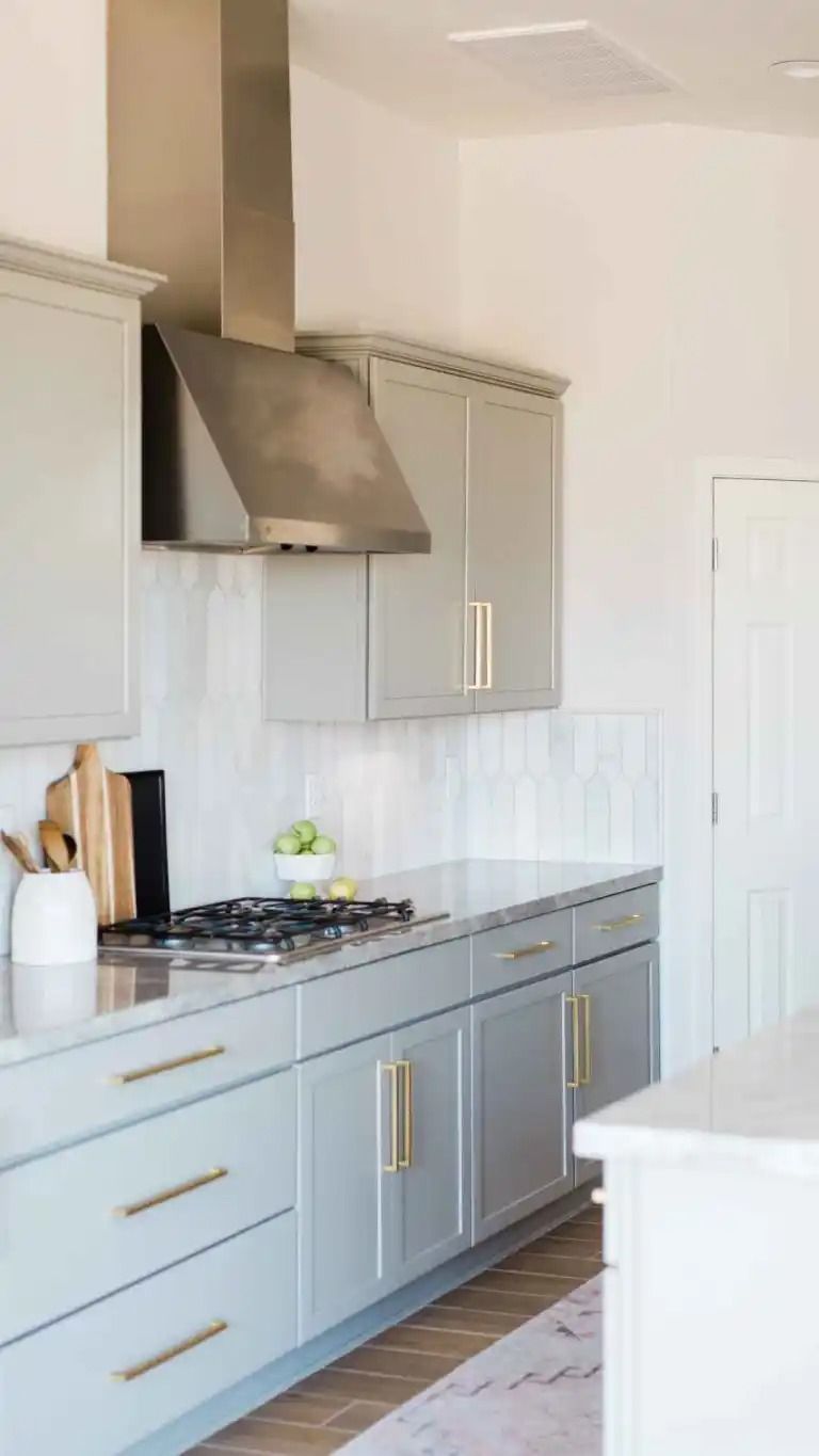 Kitchen with light gray cabinets, stainless steel range hood, marble countertop, and gold hardware.