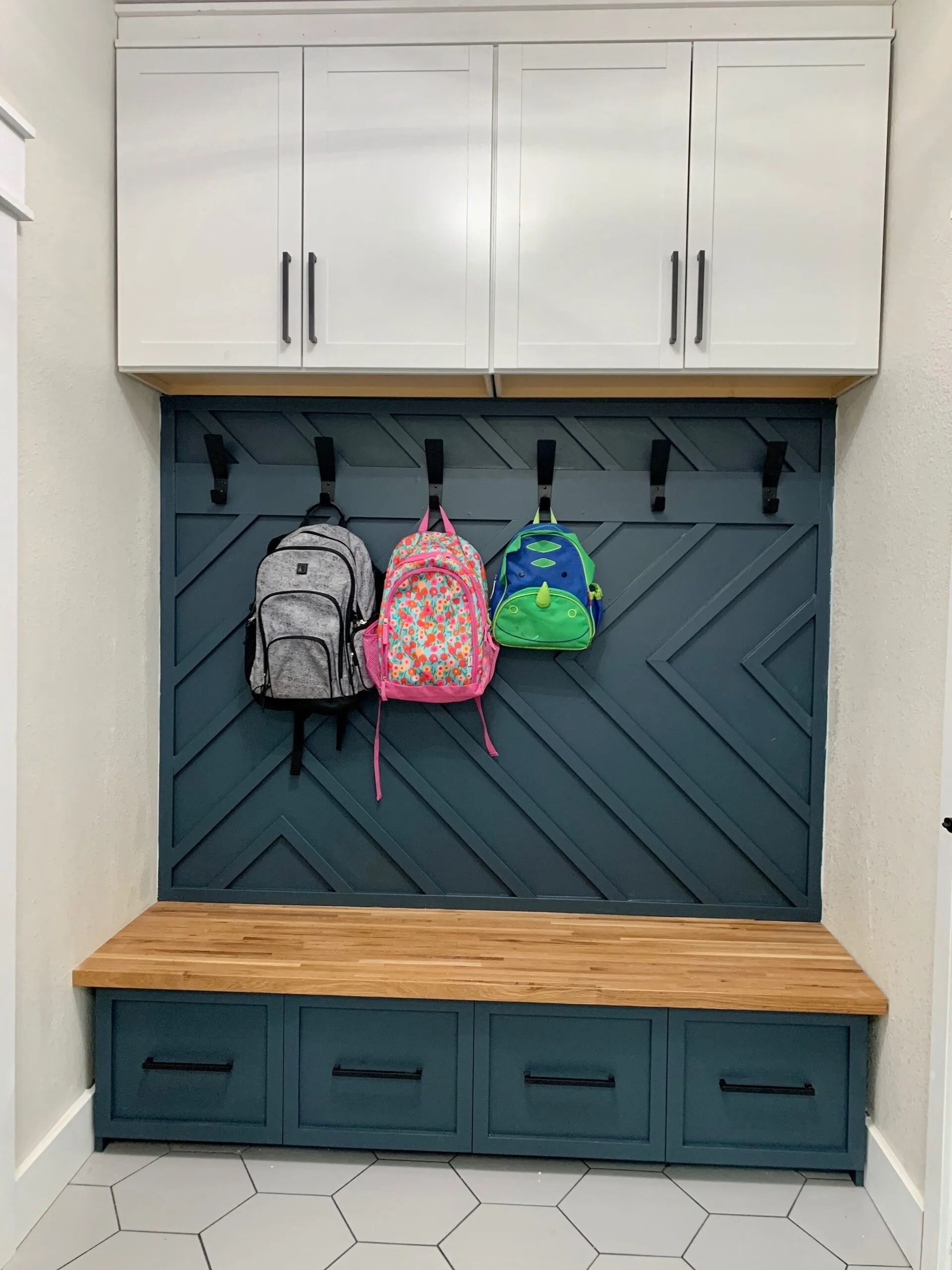 Mudroom storage: blue and wood bench with drawers, backpack hooks, and white overhead cabinets.