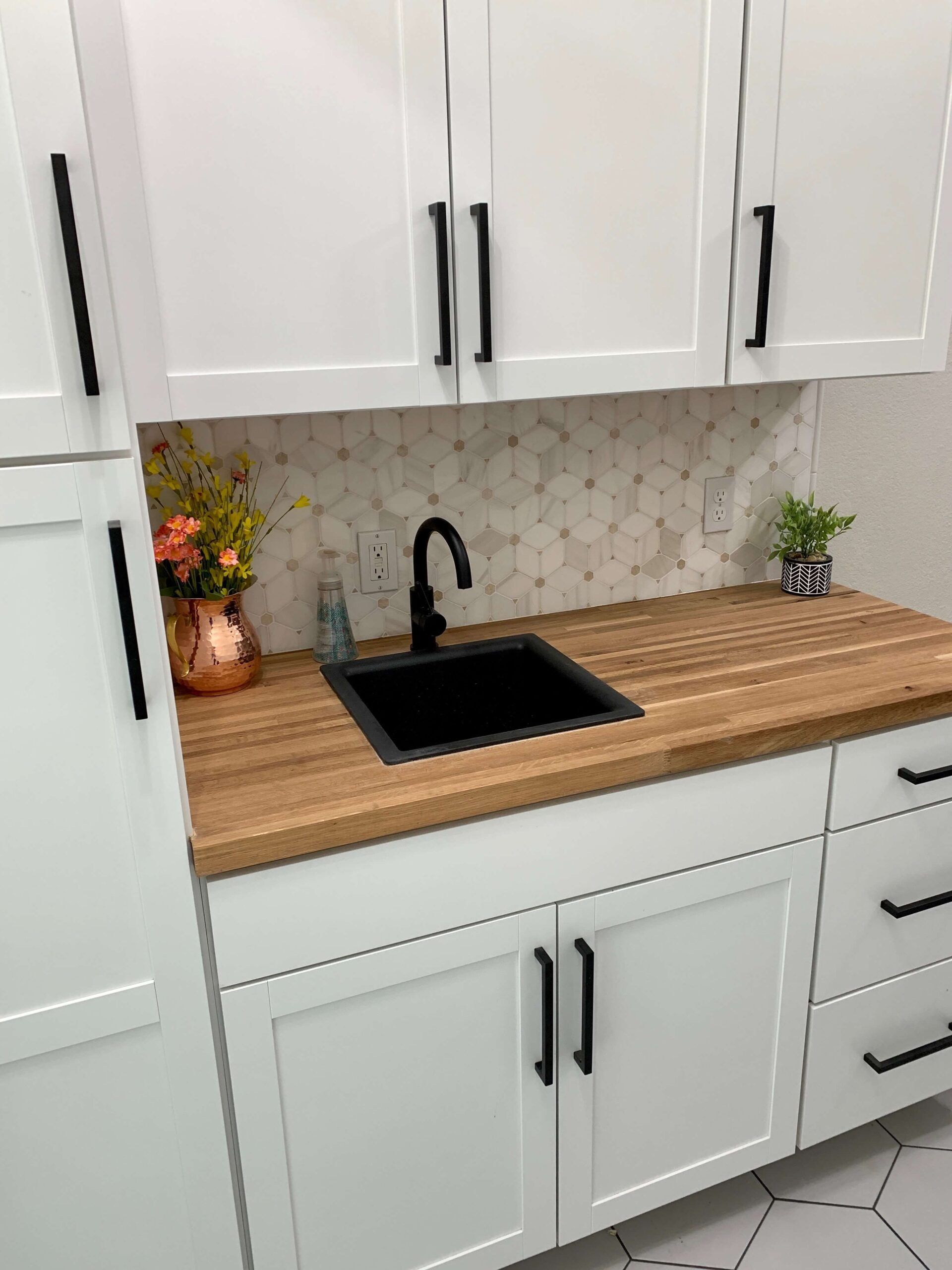 White cabinets and butcher block countertop in a utility room with a black sink and faucet.
