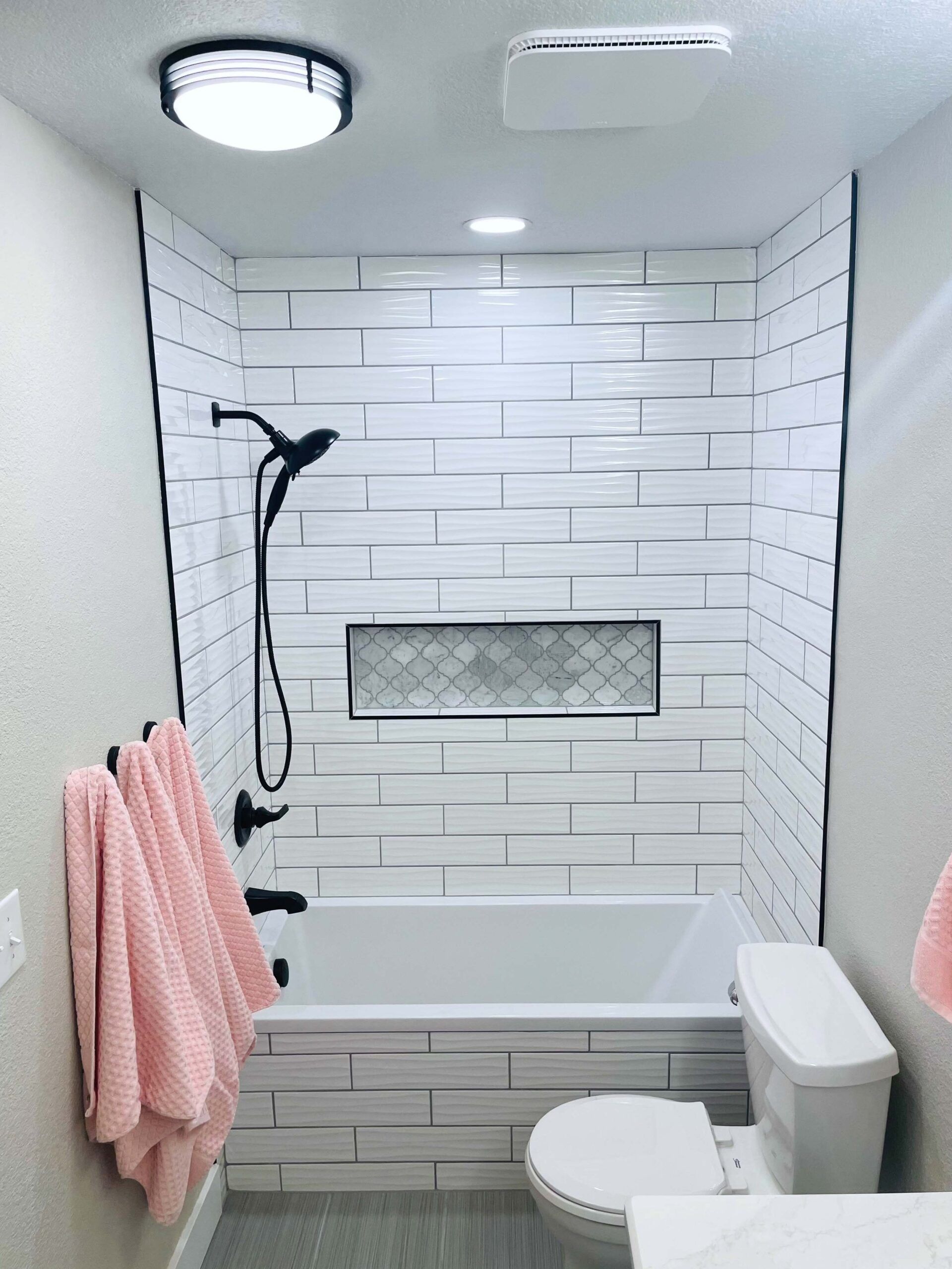 Bathroom with white subway tile, black fixtures, and pink towels.
