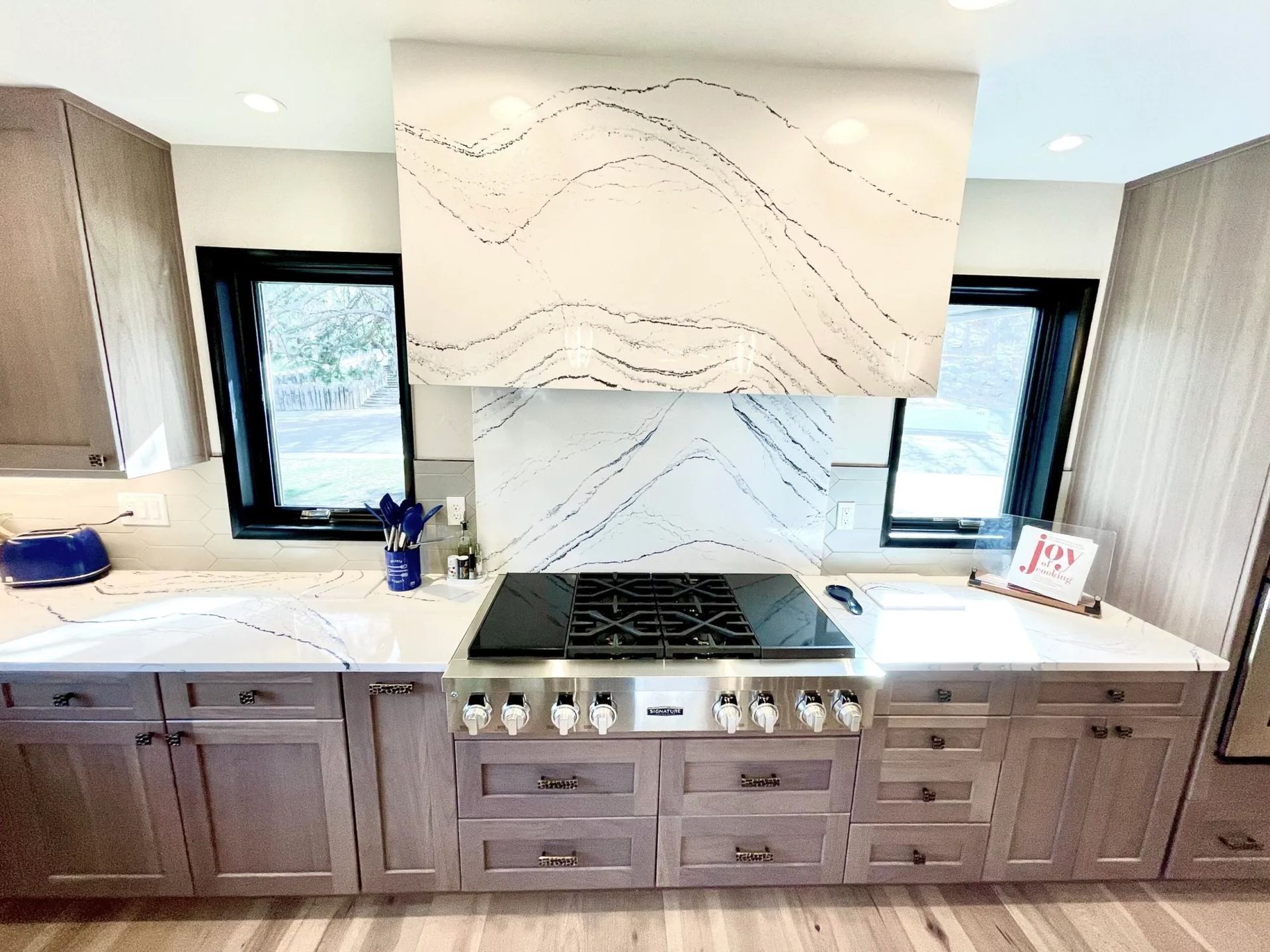 Modern kitchen with light wood cabinets, white countertops, and a range hood with a unique pattern.