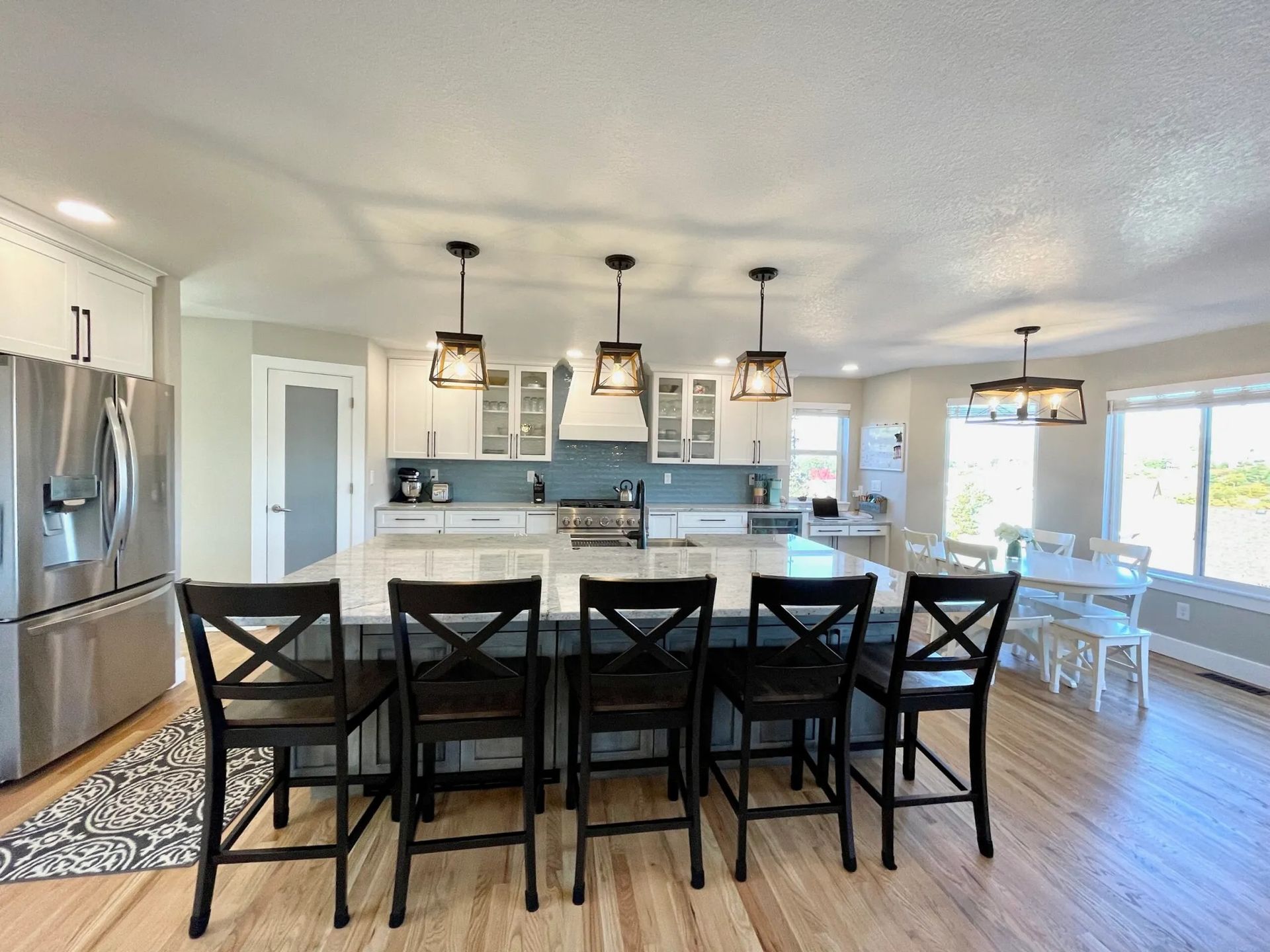 Kitchen with large island, black chairs, white cabinets, stainless steel appliances, and wood floor.