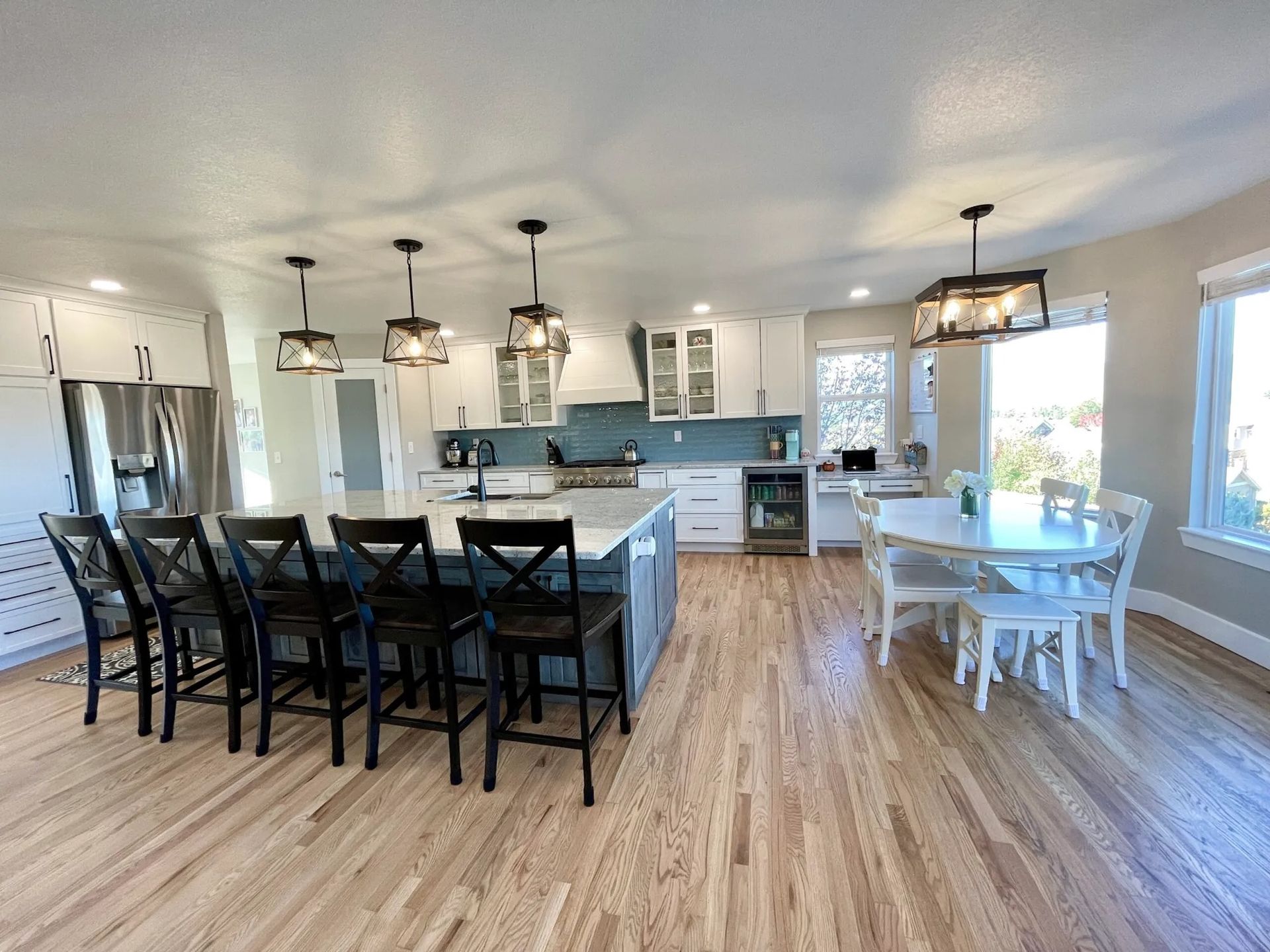 Spacious kitchen with island, seating, and dining area; wood floors, white cabinets, and blue backsplash.