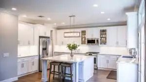 White kitchen with island, stainless steel appliances, and overhead lighting.