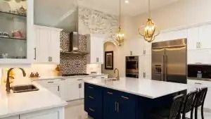 Modern kitchen with white cabinets, blue island, stainless steel appliances, and gold light fixtures.