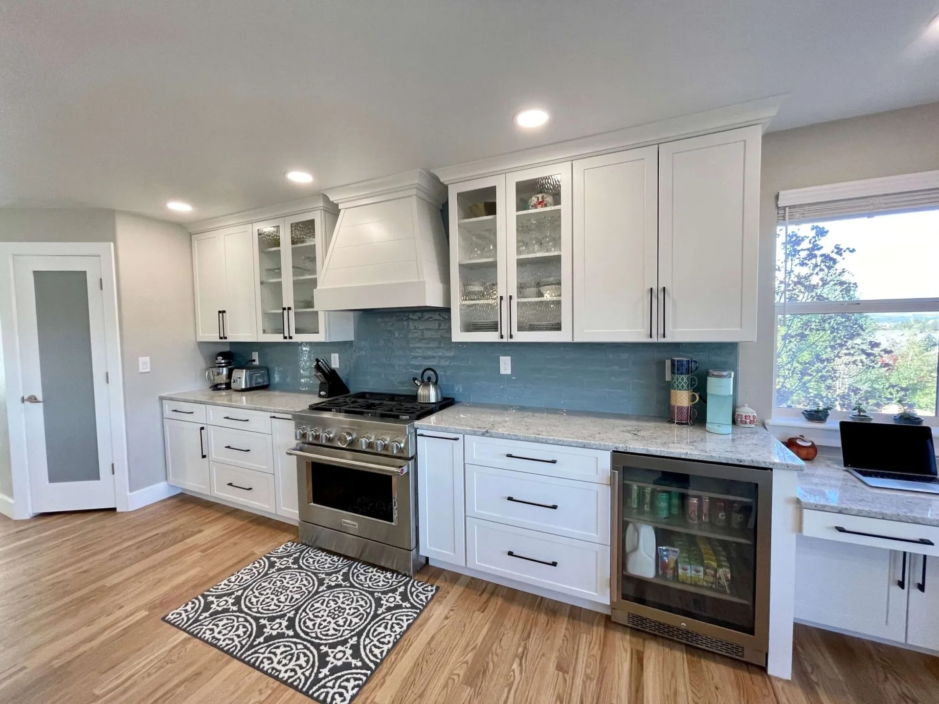 White kitchen with light wood floors, blue backsplash, and stainless steel appliances.