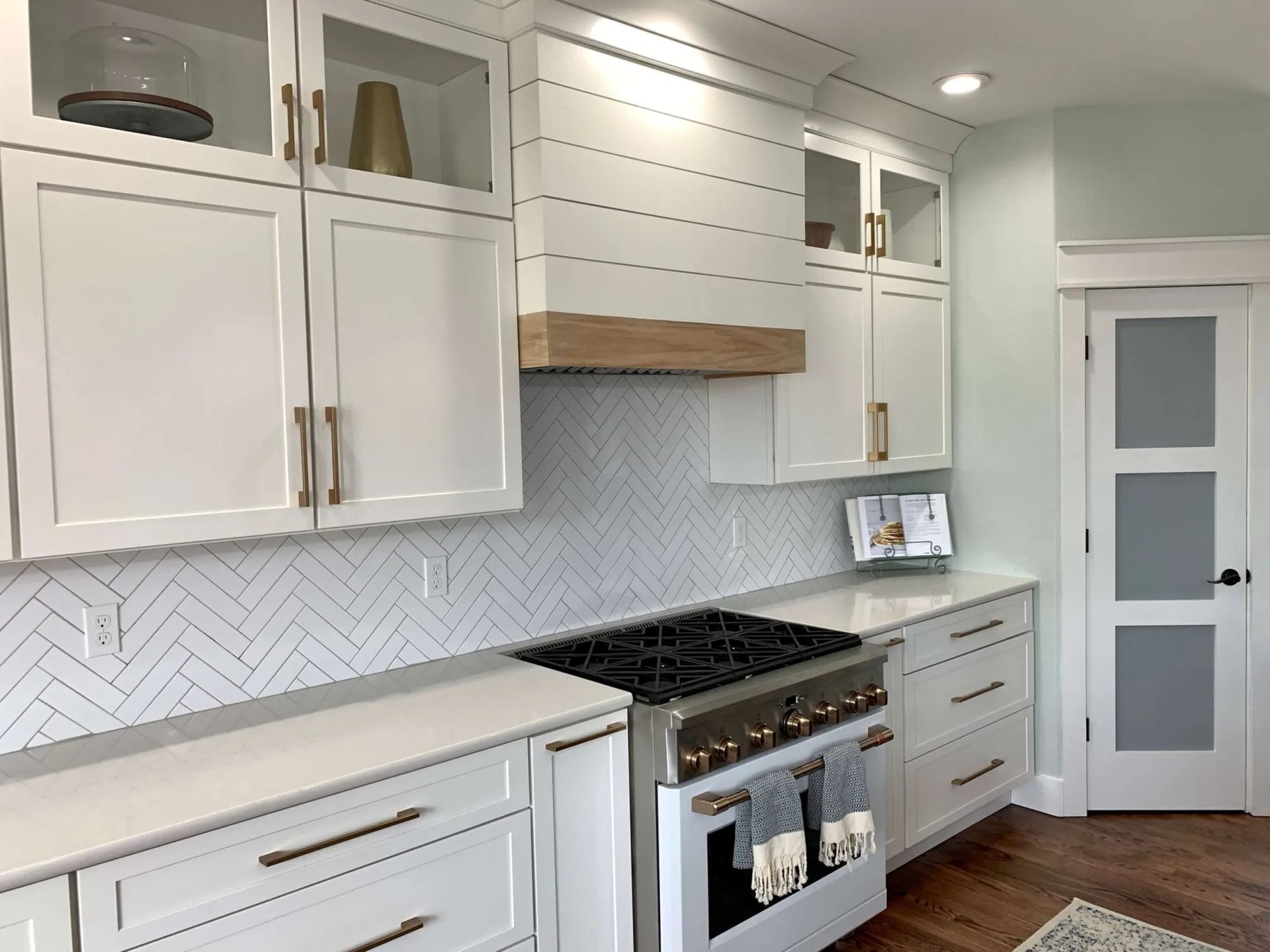 White kitchen with herringbone backsplash, cabinets, and light wood range hood.