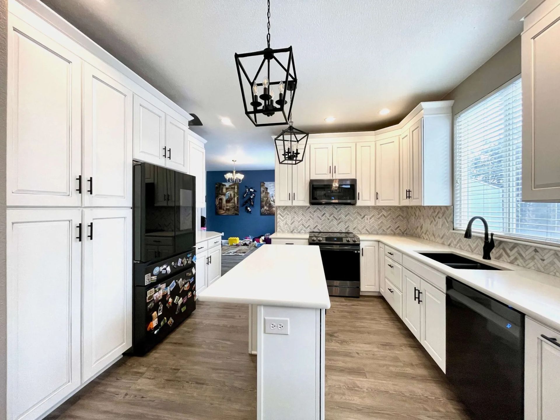 White kitchen with black appliances and cabinets, white countertops and backsplash, light wood floor.
