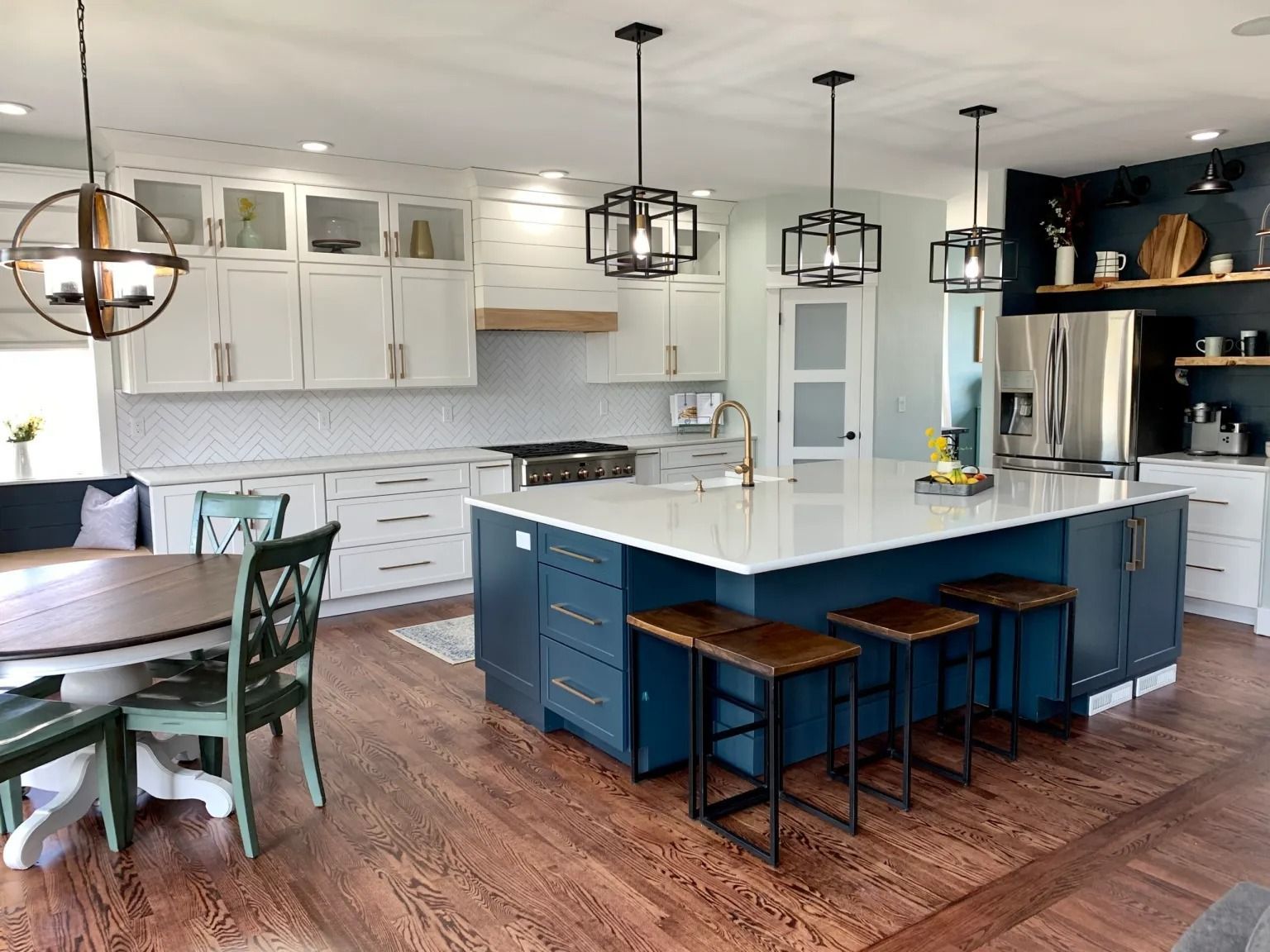 Modern kitchen with blue island and white cabinets, wood flooring and three pendant lights.
