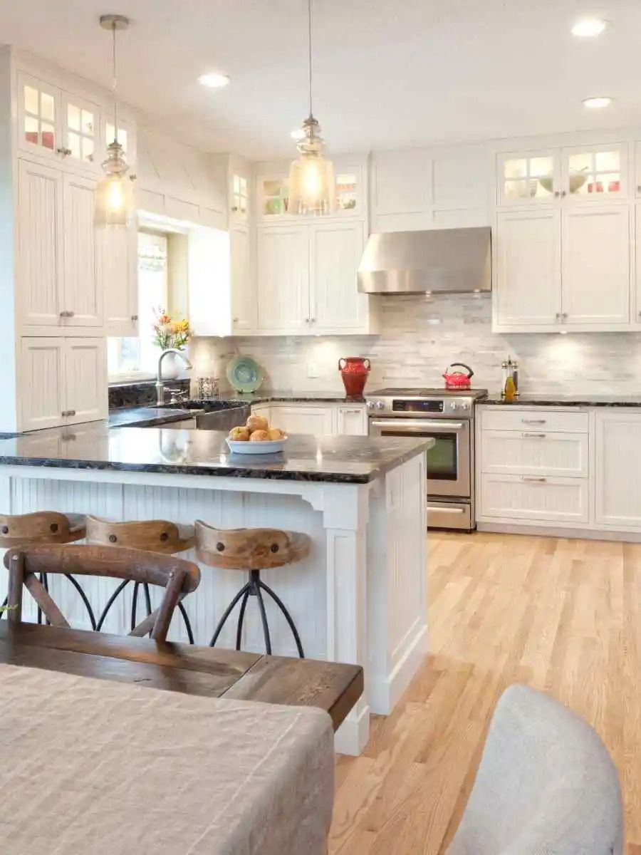 White kitchen with island, black countertop, light wood floor, and three bar stools.