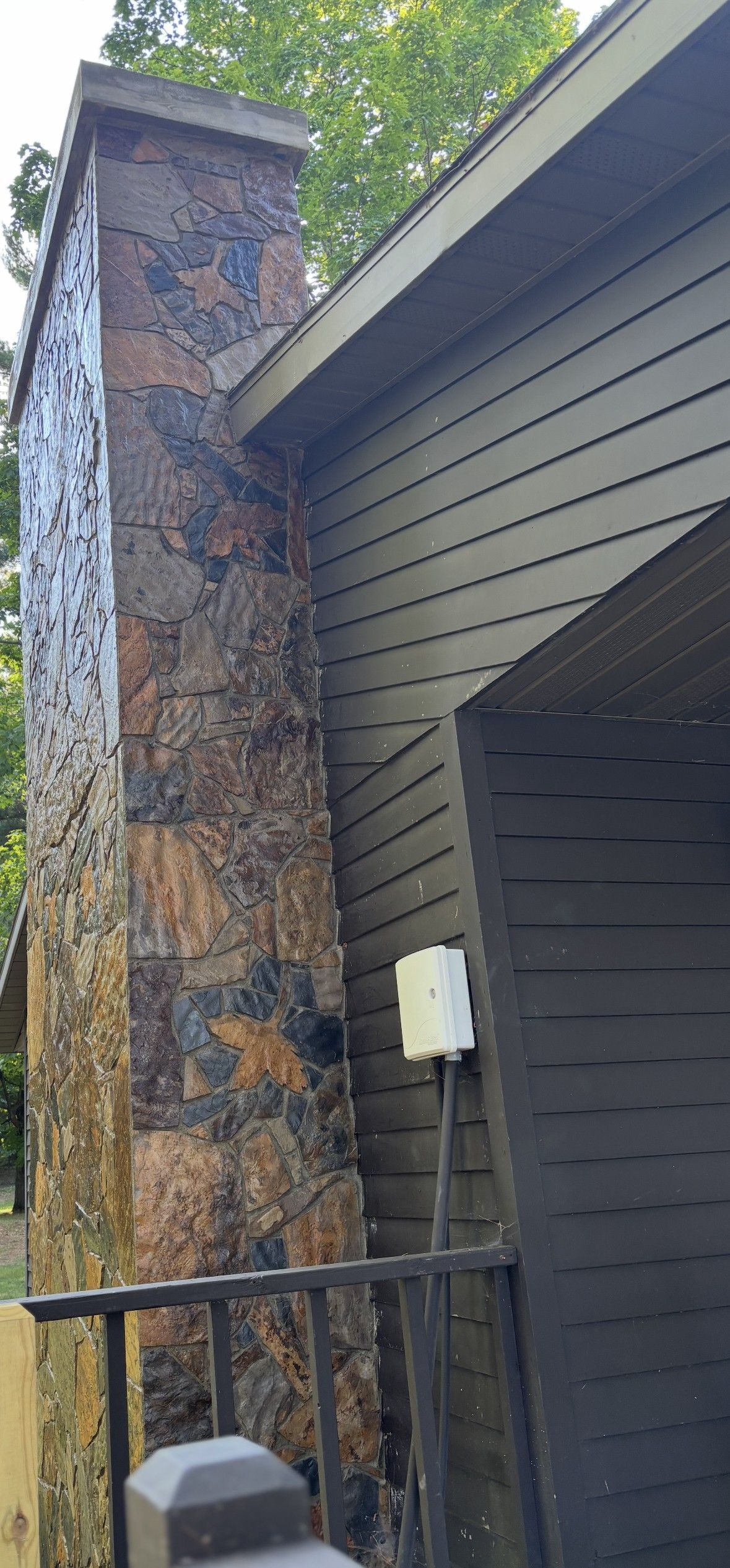 Stone chimney next to a dark-colored building, with a white electrical box on the wall.