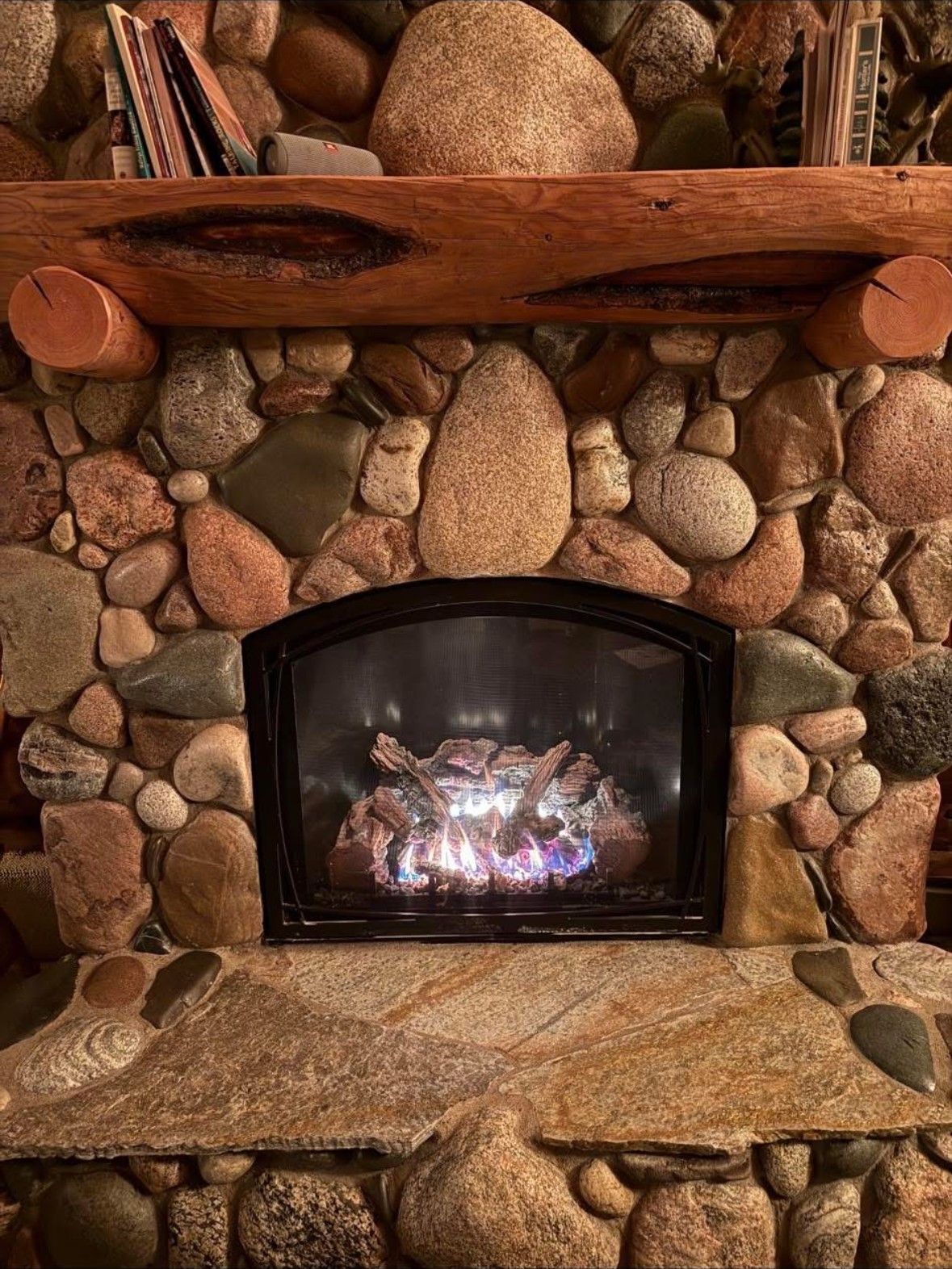 Stone fireplace with a burning fire, a wooden mantel, and books on the shelf.