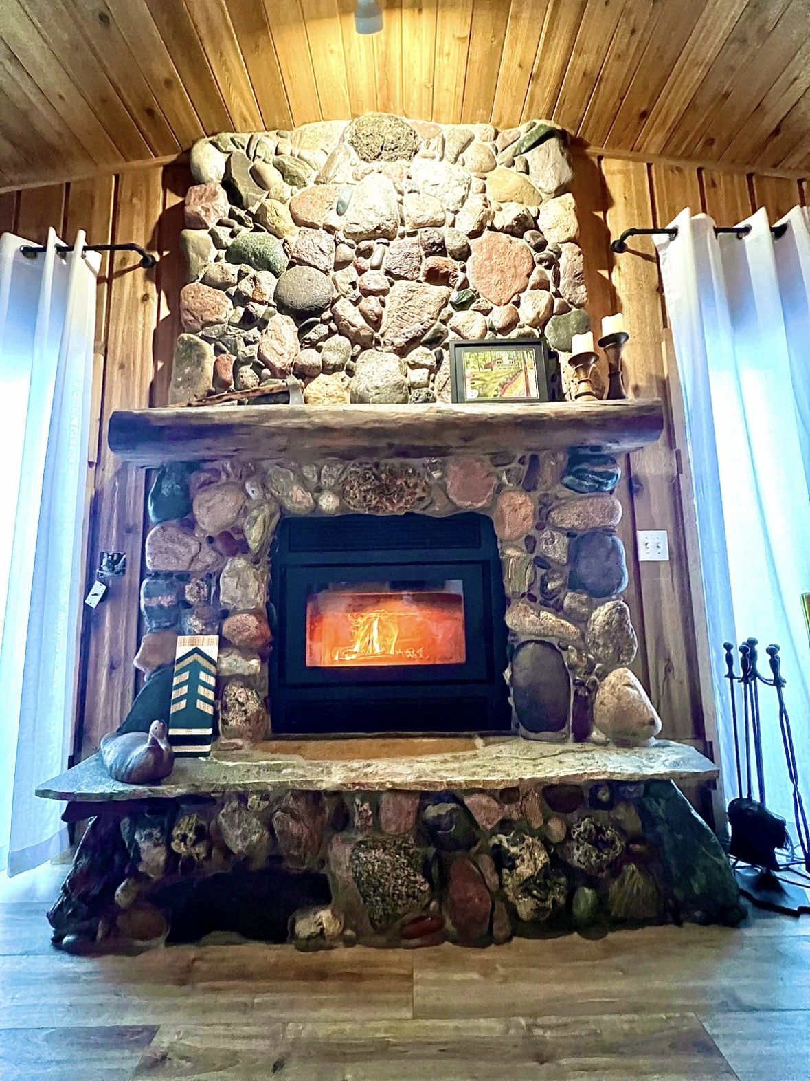 Stone fireplace with fire burning, wood mantel, and wood panel walls.