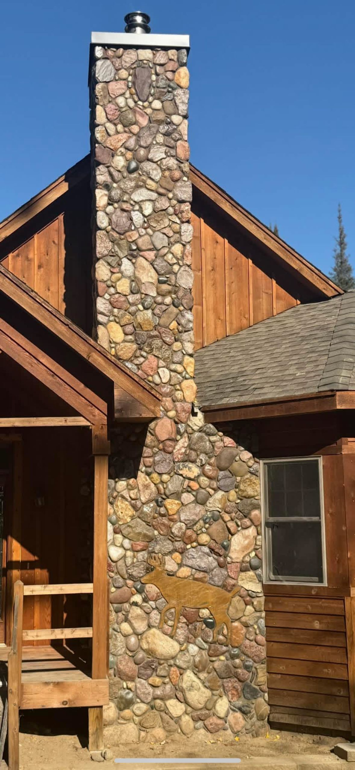 Stone chimney on a wooden house with a blue sky background.