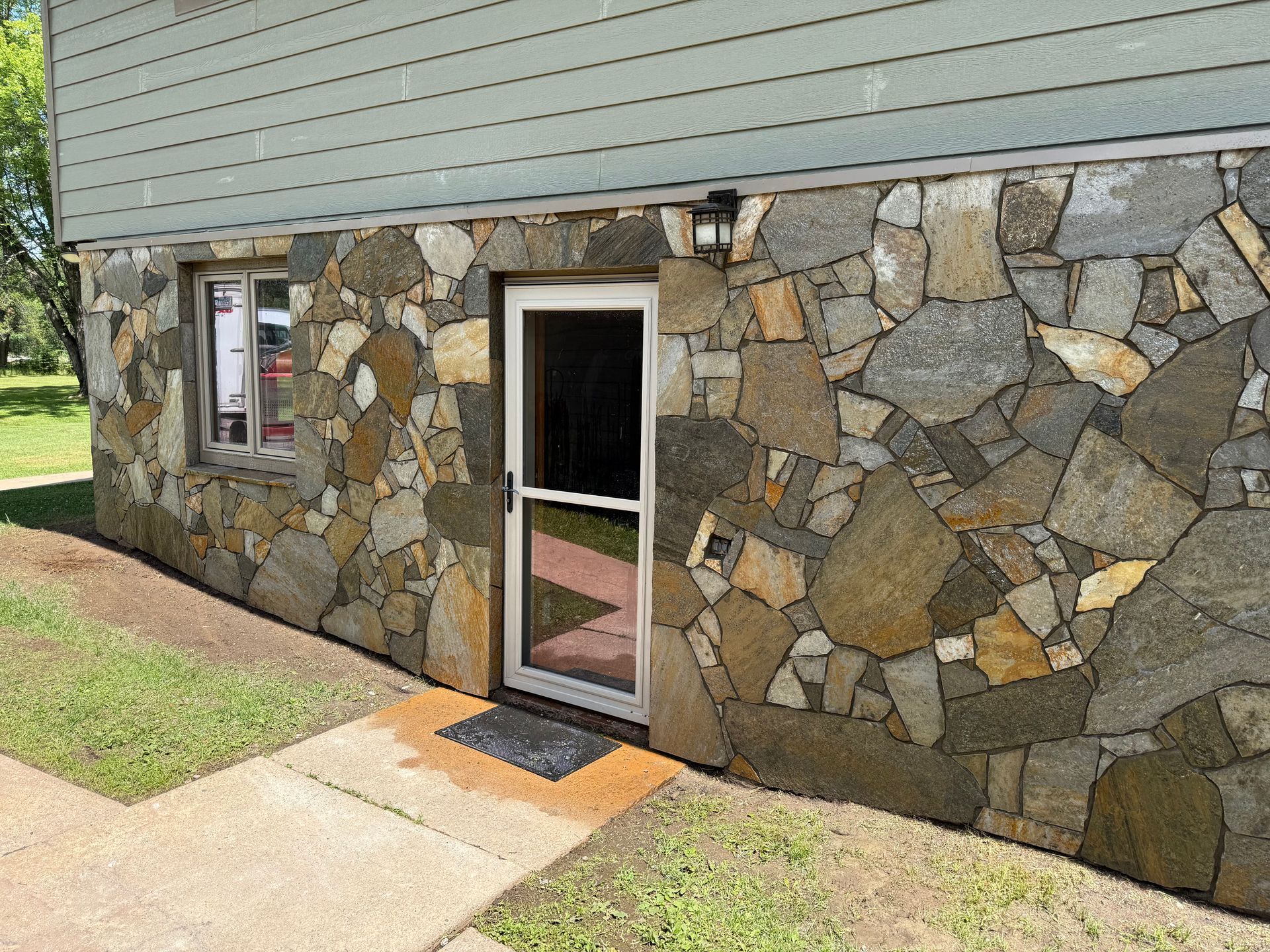 Stone wall exterior of a building with a door, window, and small porch; green grass.