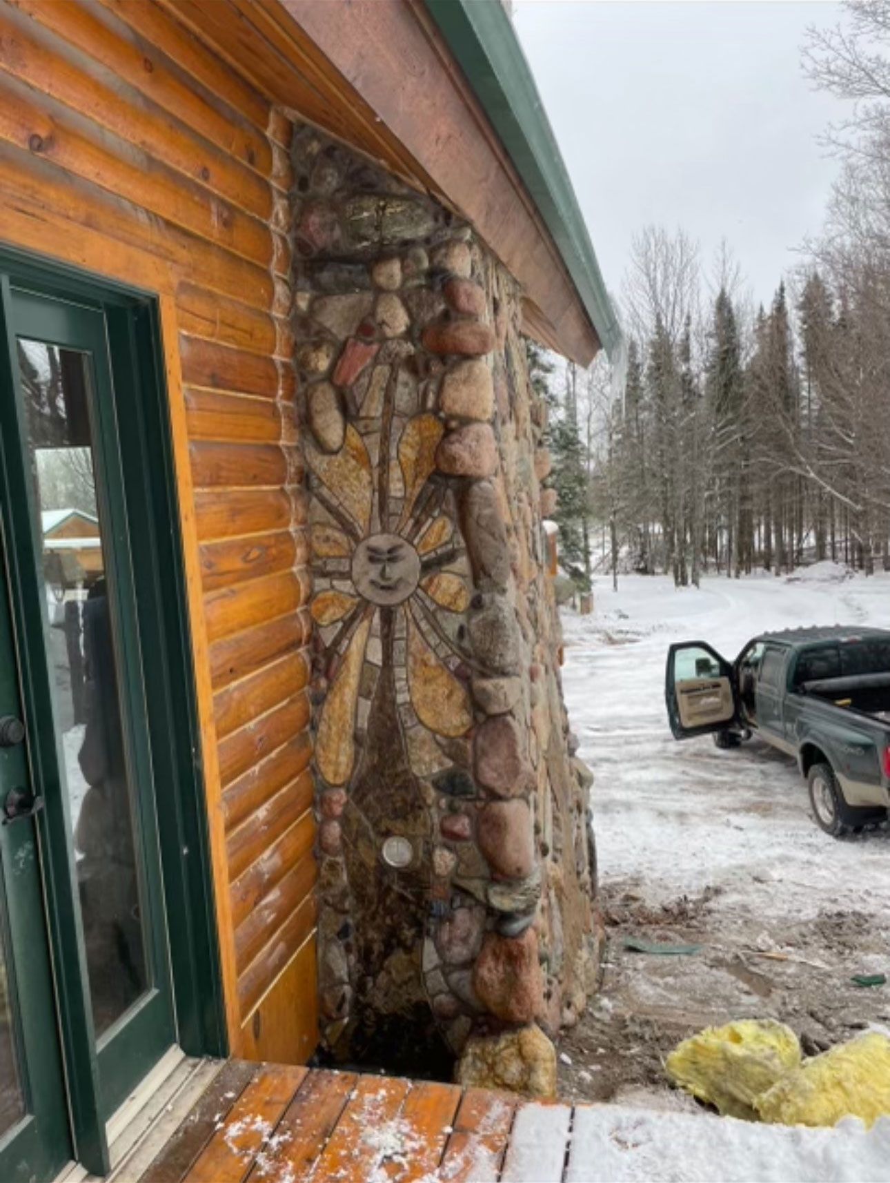 A log cabin with a stone fireplace and a truck parked in front of it