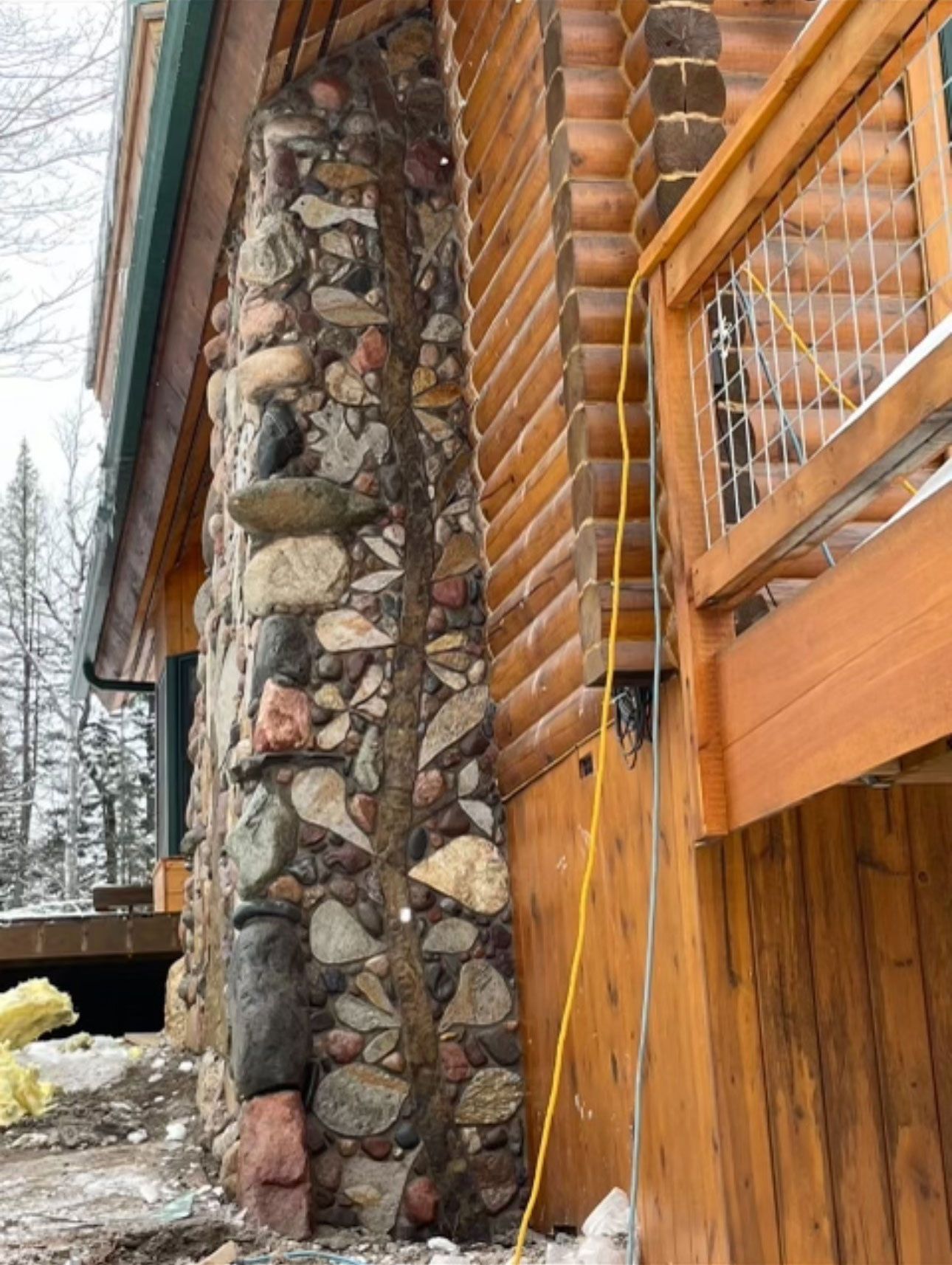 A large stone chimney on the side of a log cabin