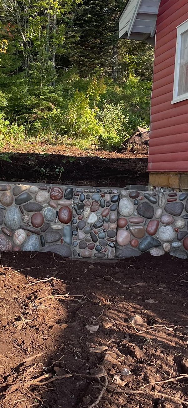 A stone wall is being built in front of a red house.