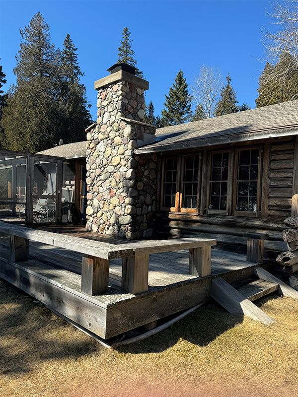 A log cabin with a stone chimney and a wooden deck.