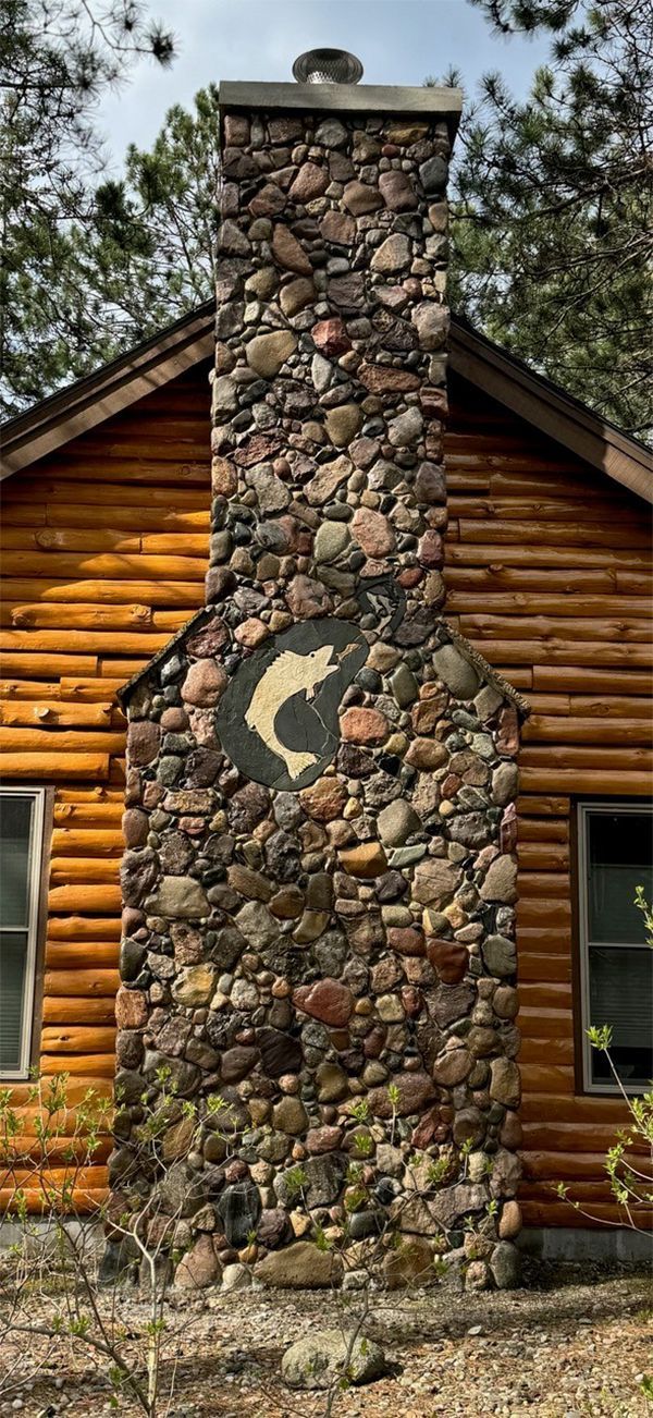 A log cabin with a stone chimney on the side of it.