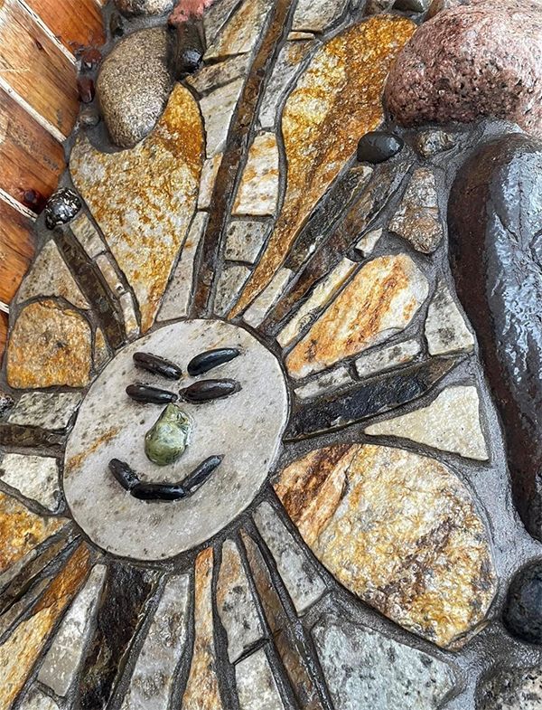 A stone mosaic of a sun with a face on it.