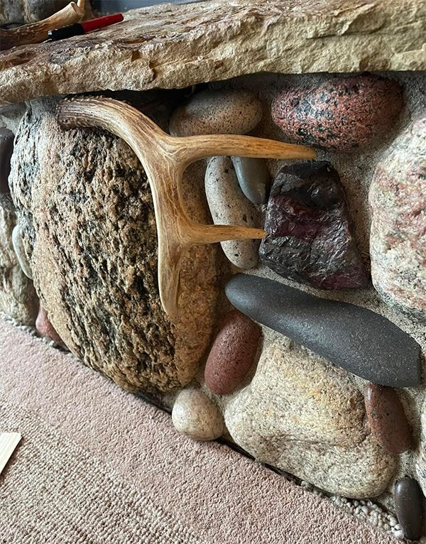 A wooden antler is sitting on top of a rock wall.