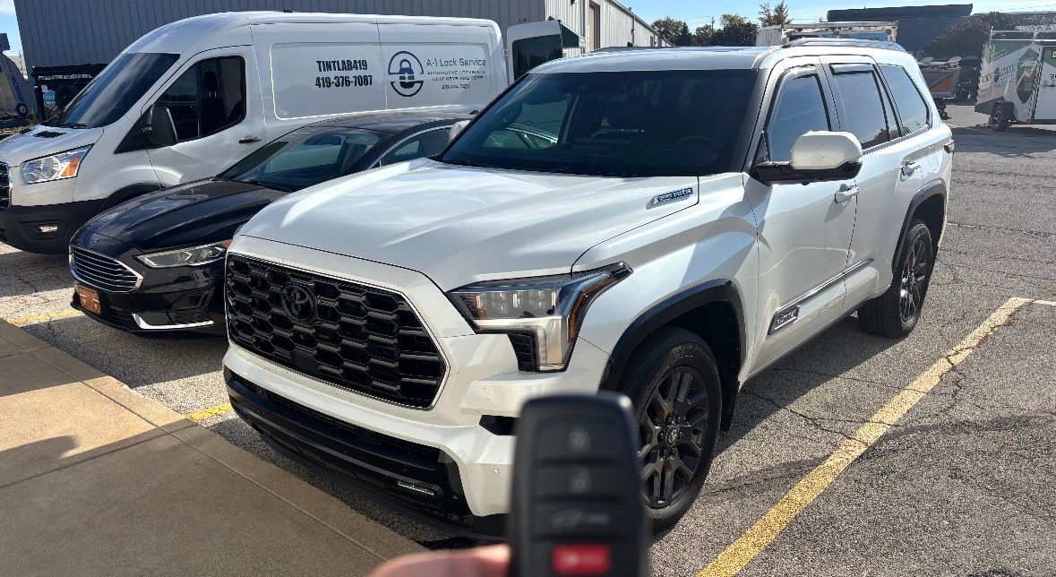 Silver SUV parked in a lot, with a van beside it and a car key fob held in the foreground.