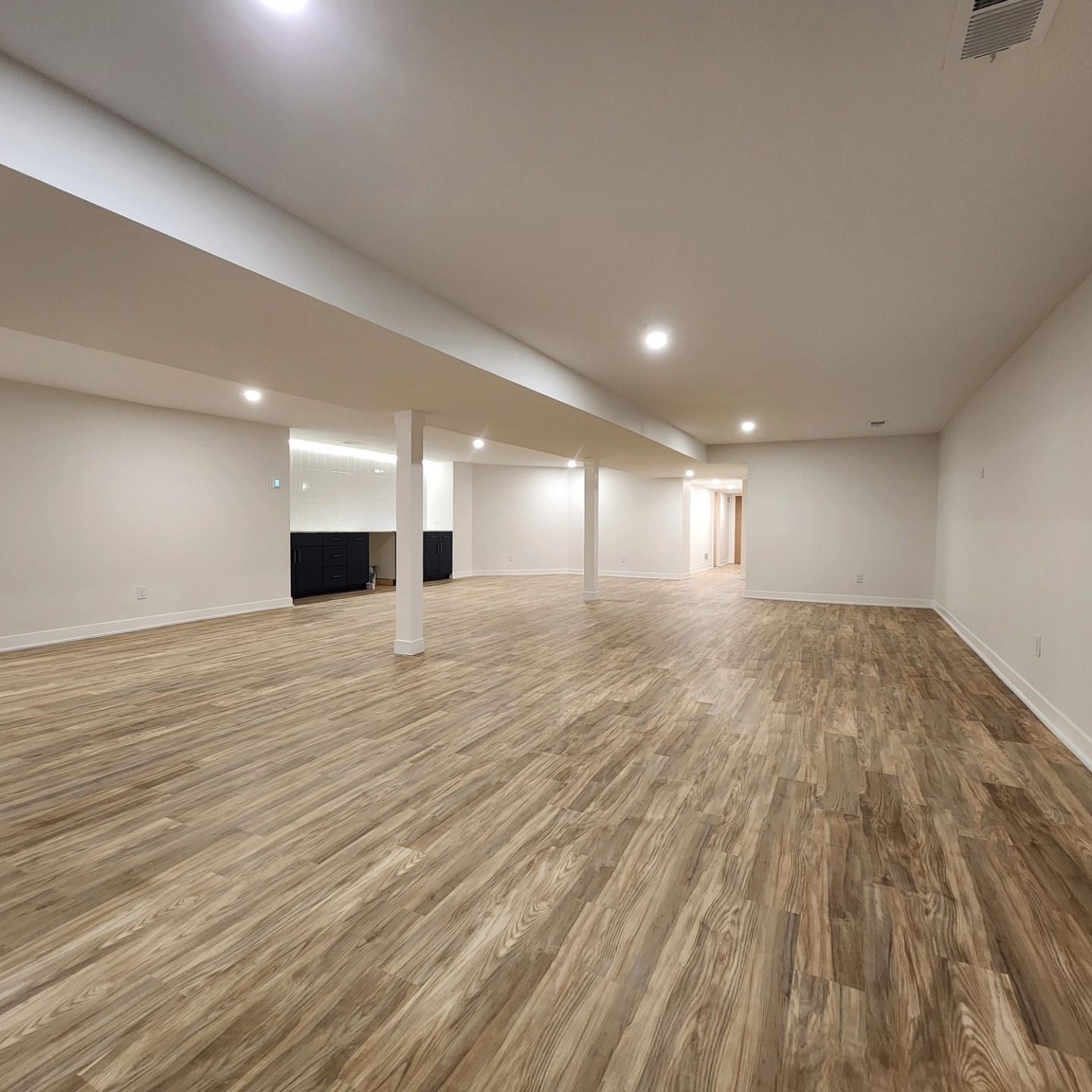 An empty basement with wooden floors and white walls.