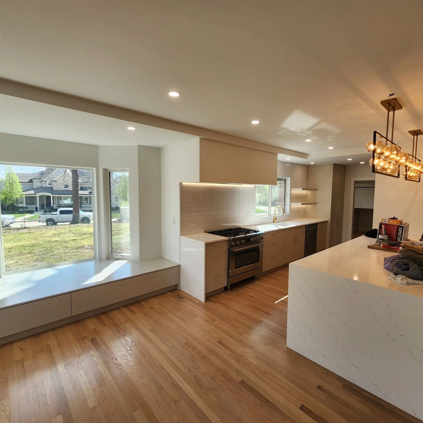 A kitchen with hardwood floors , white cabinets , a stove and a window.