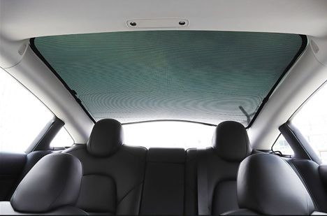 Interior view of a car's rear seats and sunroof with a mesh sunshade deployed.