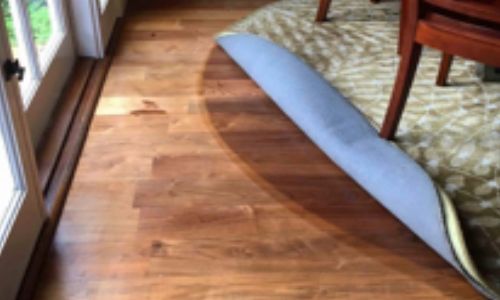 Hardwood floor with a rolled-up rug. A door and a chair leg are visible.