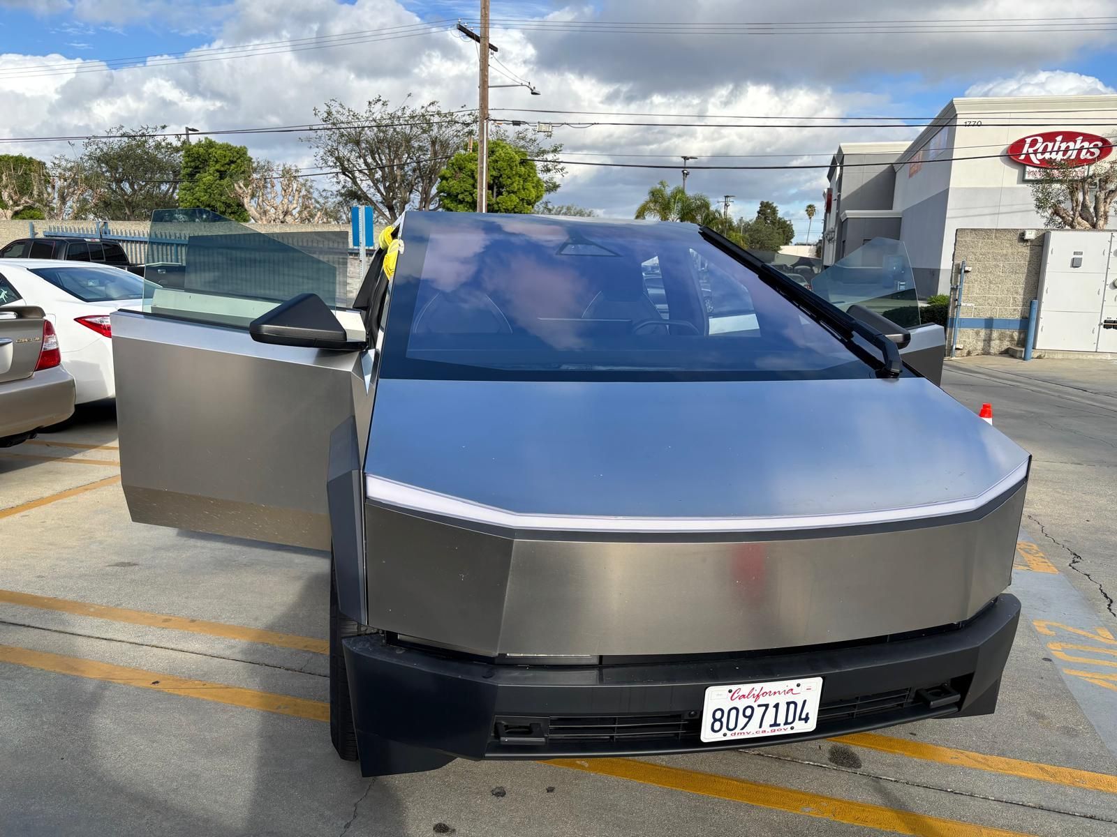 Tesla Cybertruck with door open parked in a lot, sunny day.