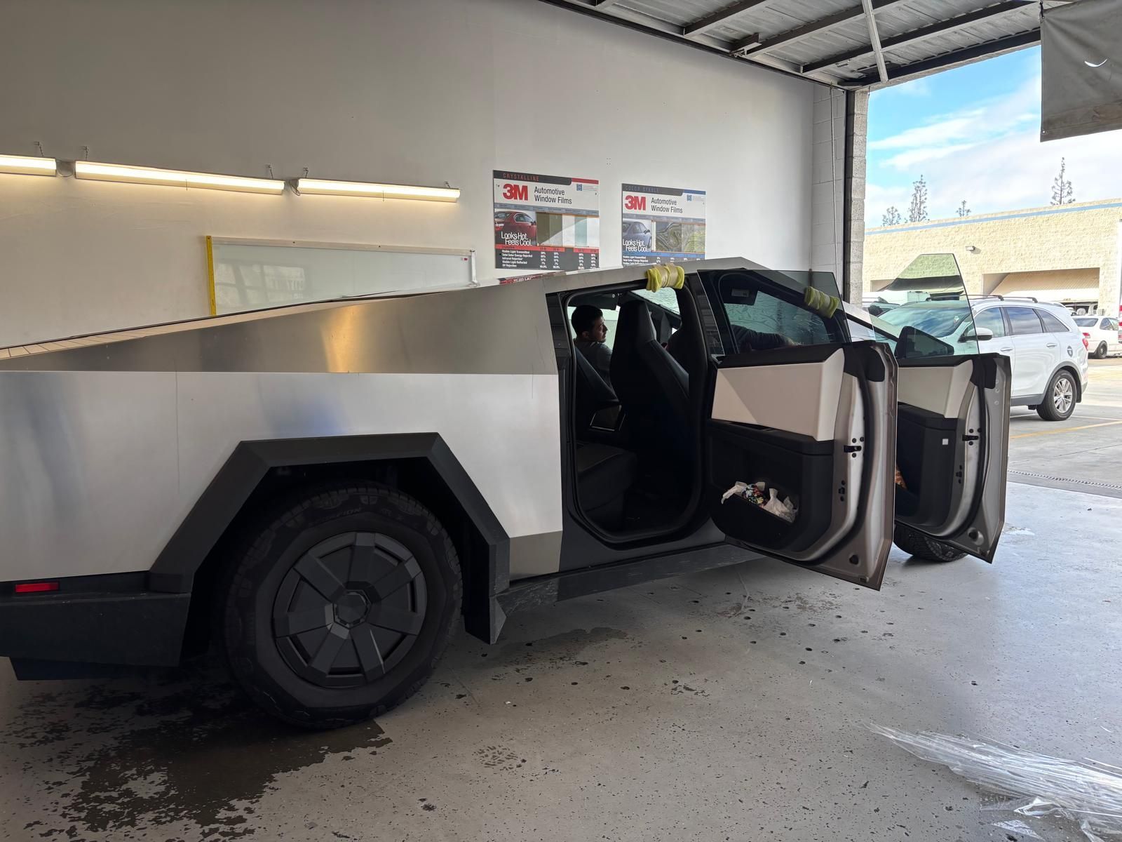 Tesla Cybertruck with open doors in a car wash bay. Stainless steel body, dark wheels.
