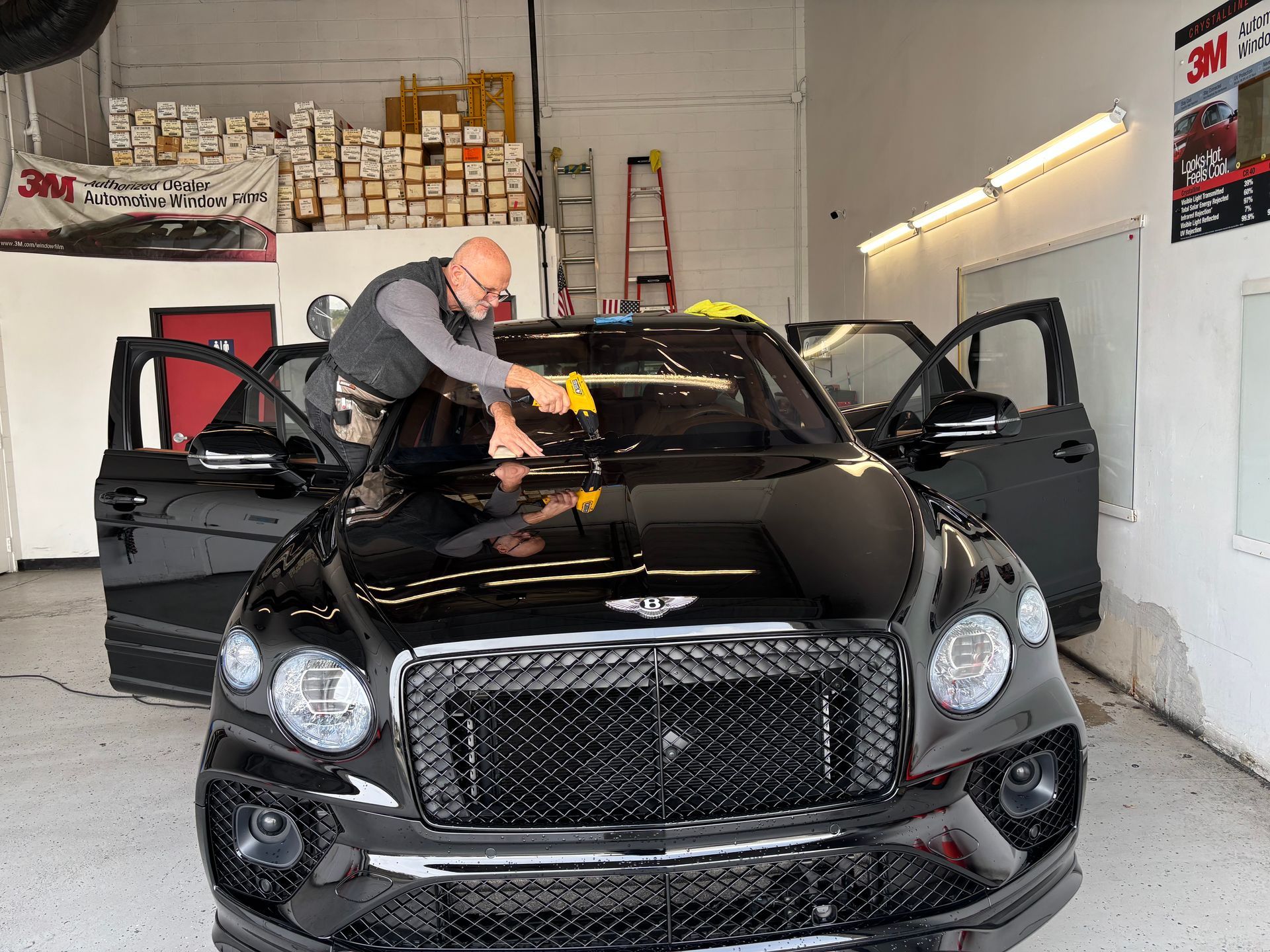 Man installing window tint on black Bentley SUV in a shop.