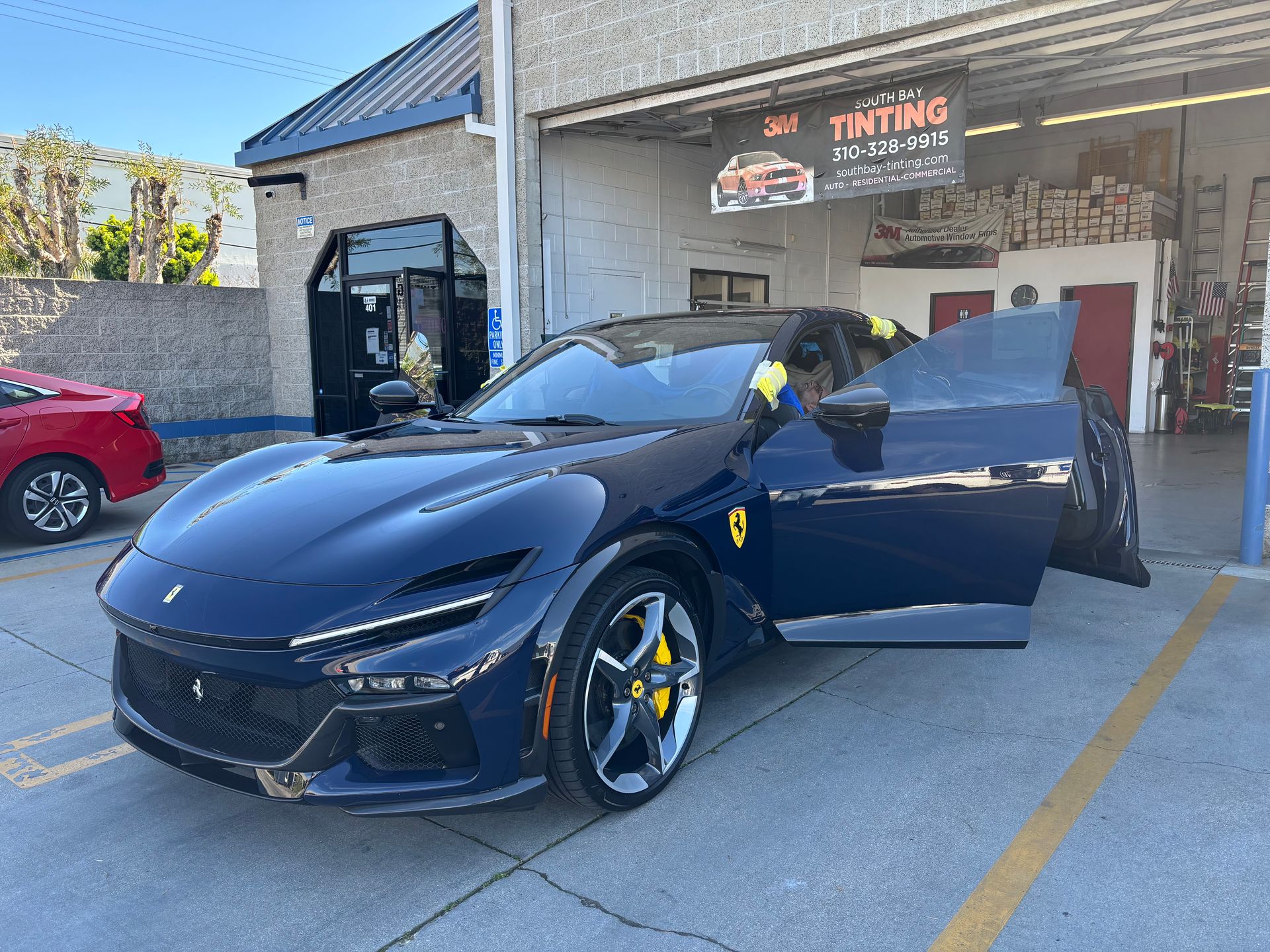 Dark blue Ferrari SUV with open doors at a tinting shop.