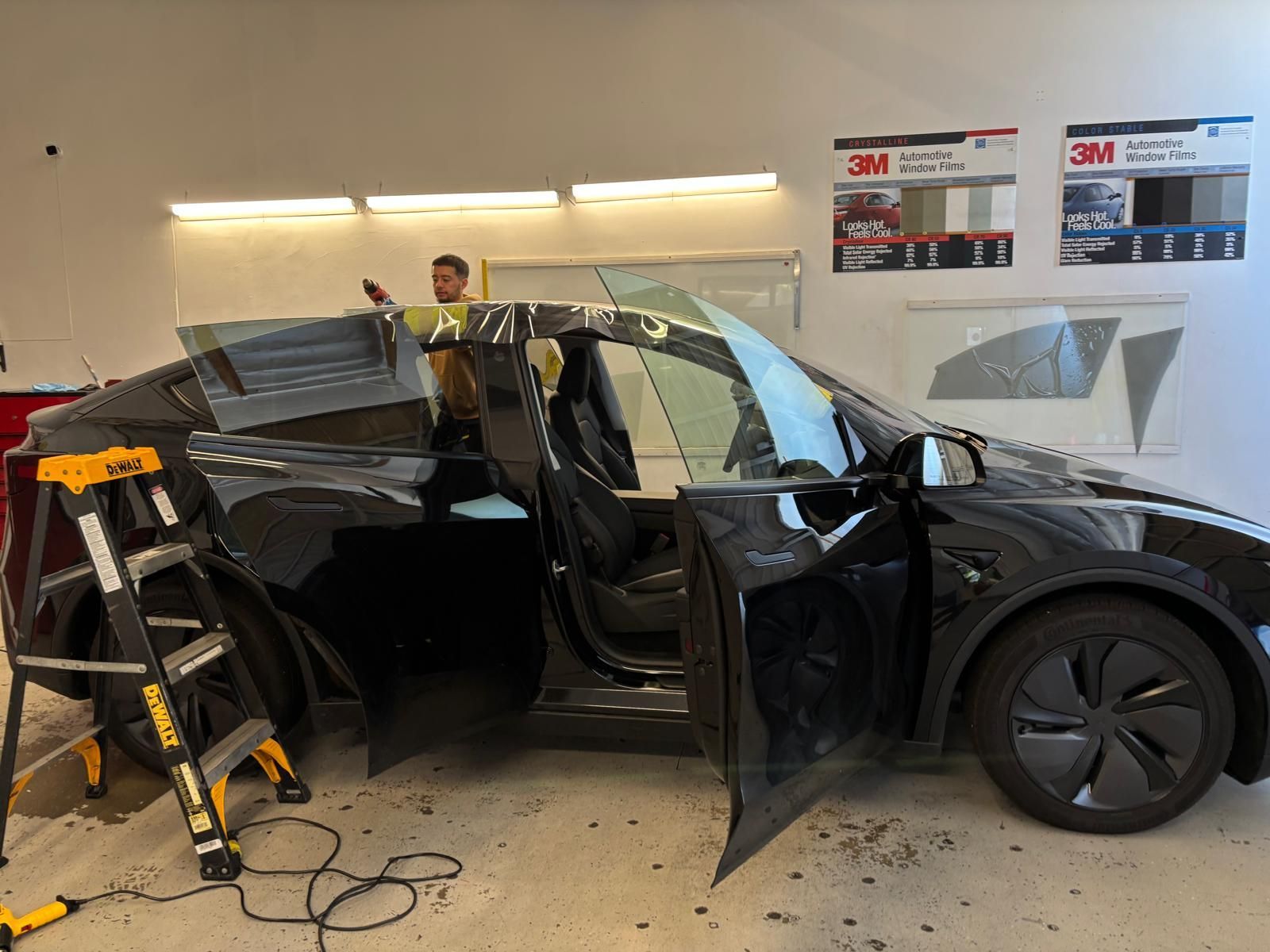 A black Tesla being tinted in a shop. A person is installing tint on the window.