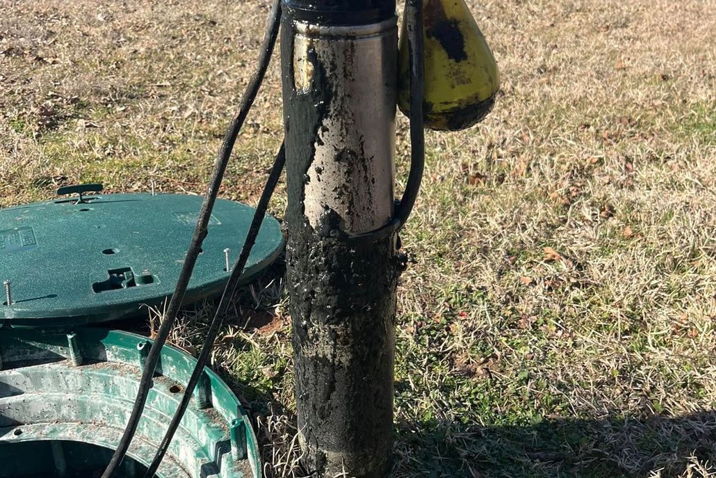 Septic tank riser with grime, electrical cord, and float; green lid in grass.
