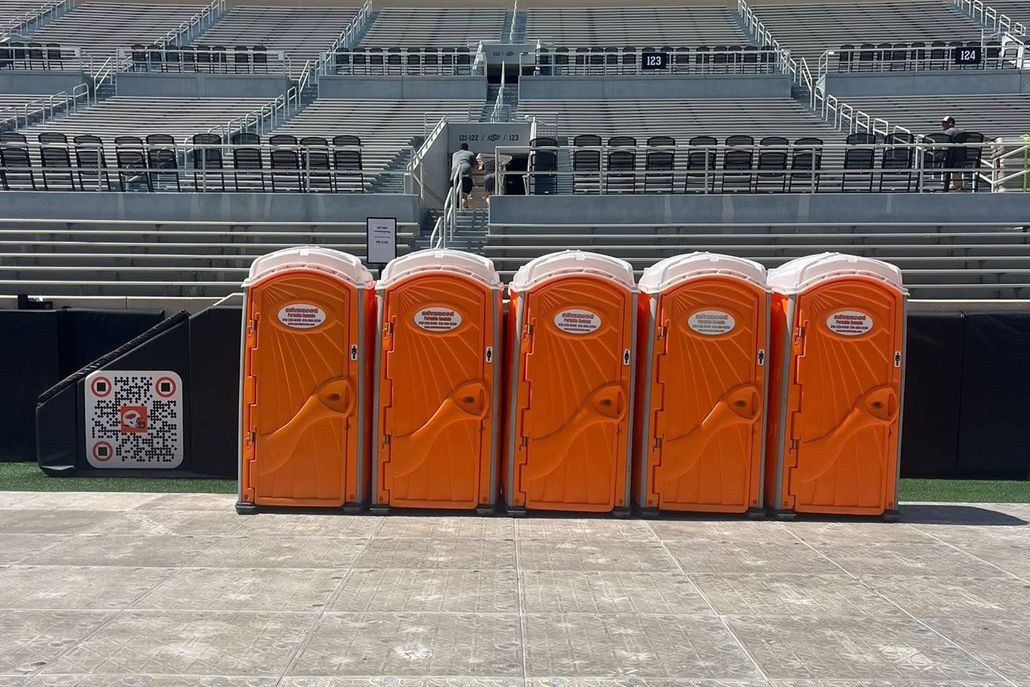 Five orange portable toilets in front of stadium seating.