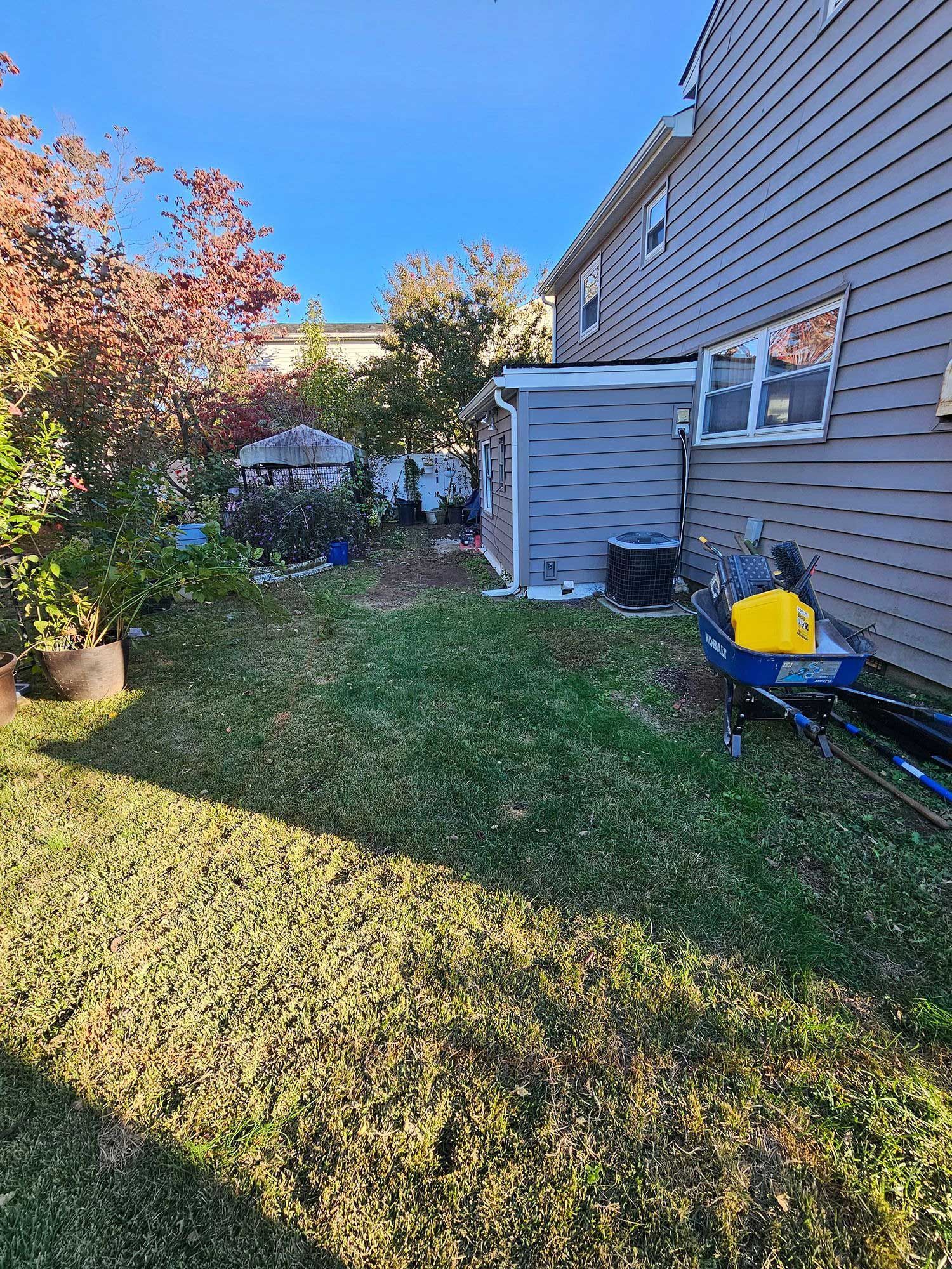A residential backyard featuring a grass lawn, trees, and a house exterior with a yellow tool cart on the side.