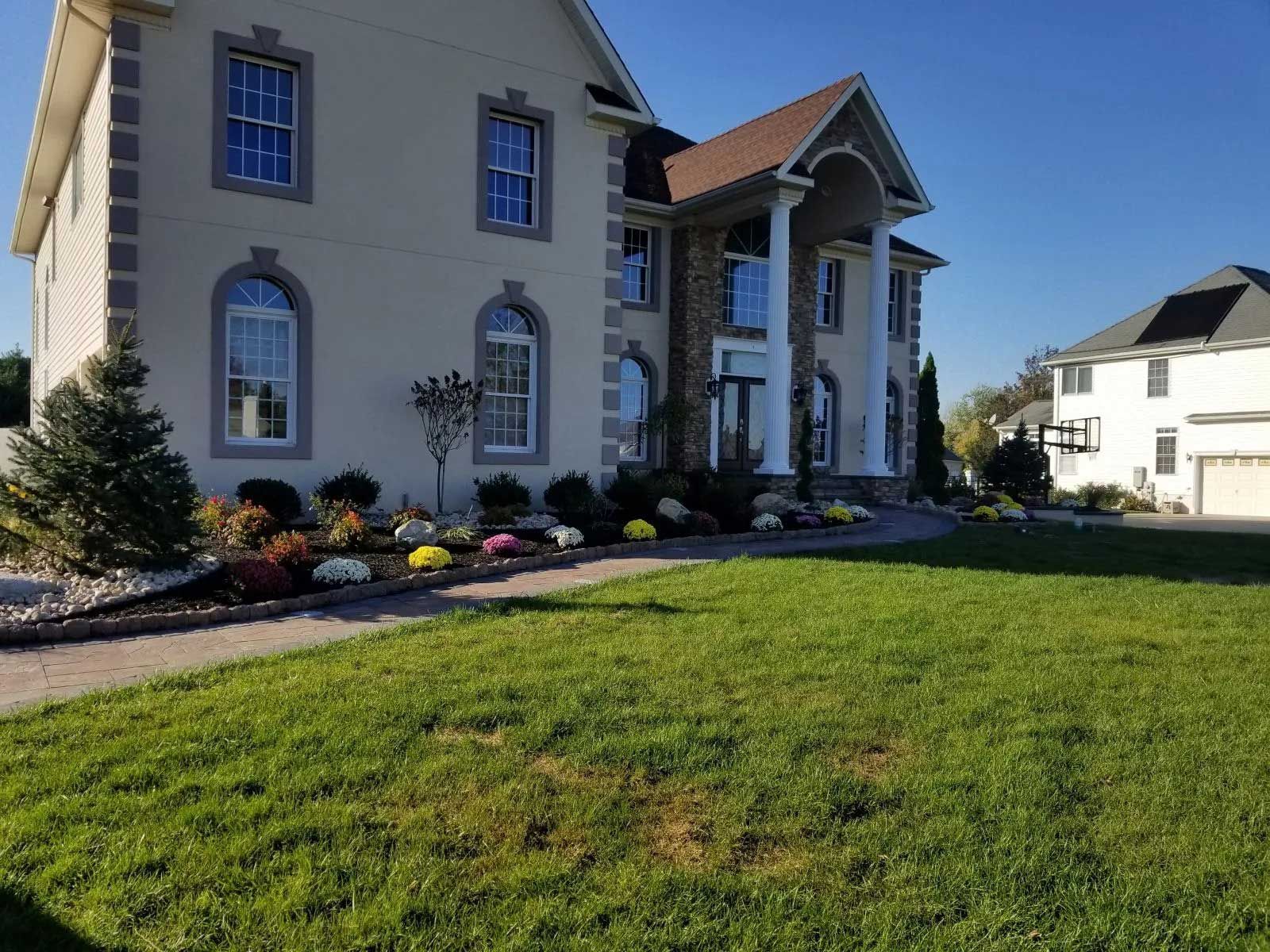 A large, two-story house with white siding, stone accents, and a front porch with tall columns, viewed from a lawn.
