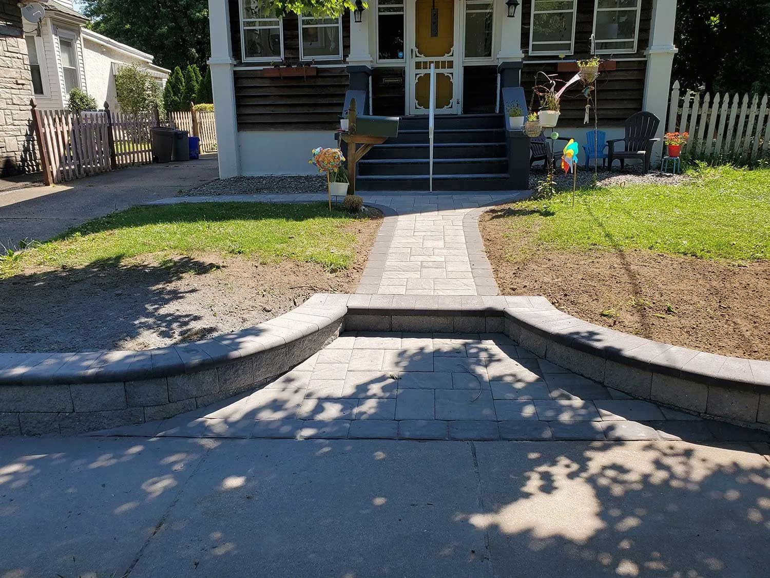 A paved path leads from a driveway up a single step and along a walkway toward the front porch of a house.