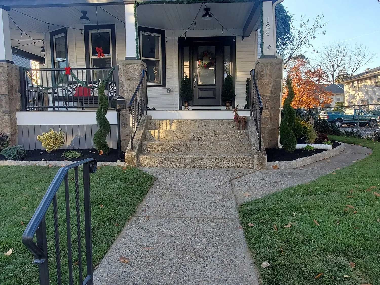 A white house with a covered front porch, stone pillars, and concrete stairs leading to a dark-framed front door.