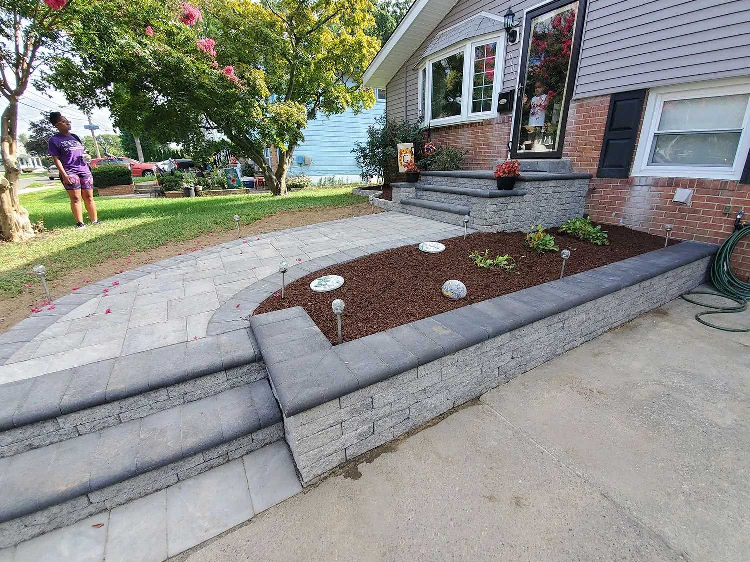 A newly installed stone retaining wall with steps and paver walkway leading to a house entrance.