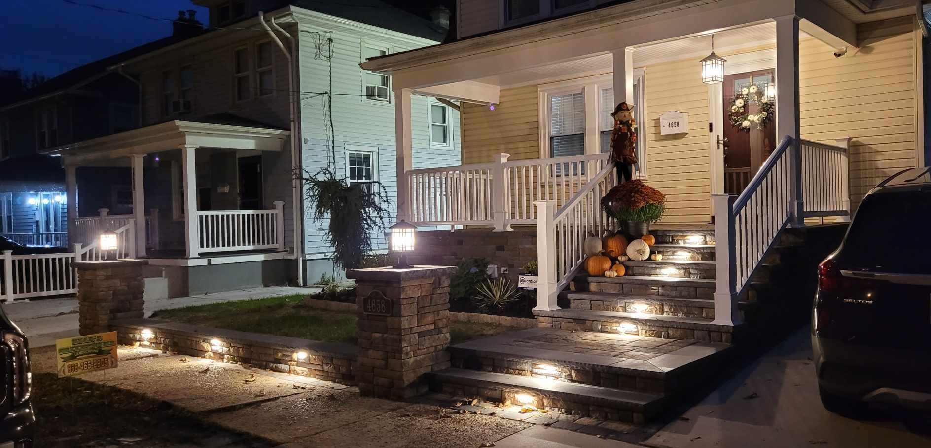 A two-story house at twilight with glowing landscape path lights illuminating stone steps, porch, and walkway.
