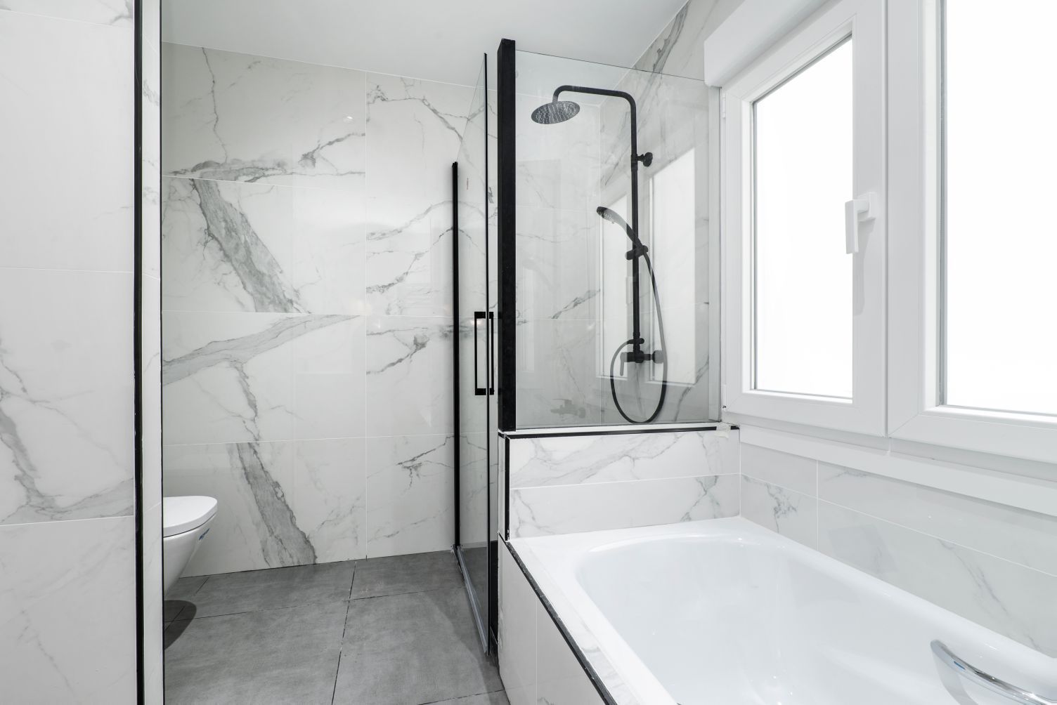 A modern bathroom featuring a white bathtub, a glass-enclosed shower with black fixtures, and marble-patterned walls.